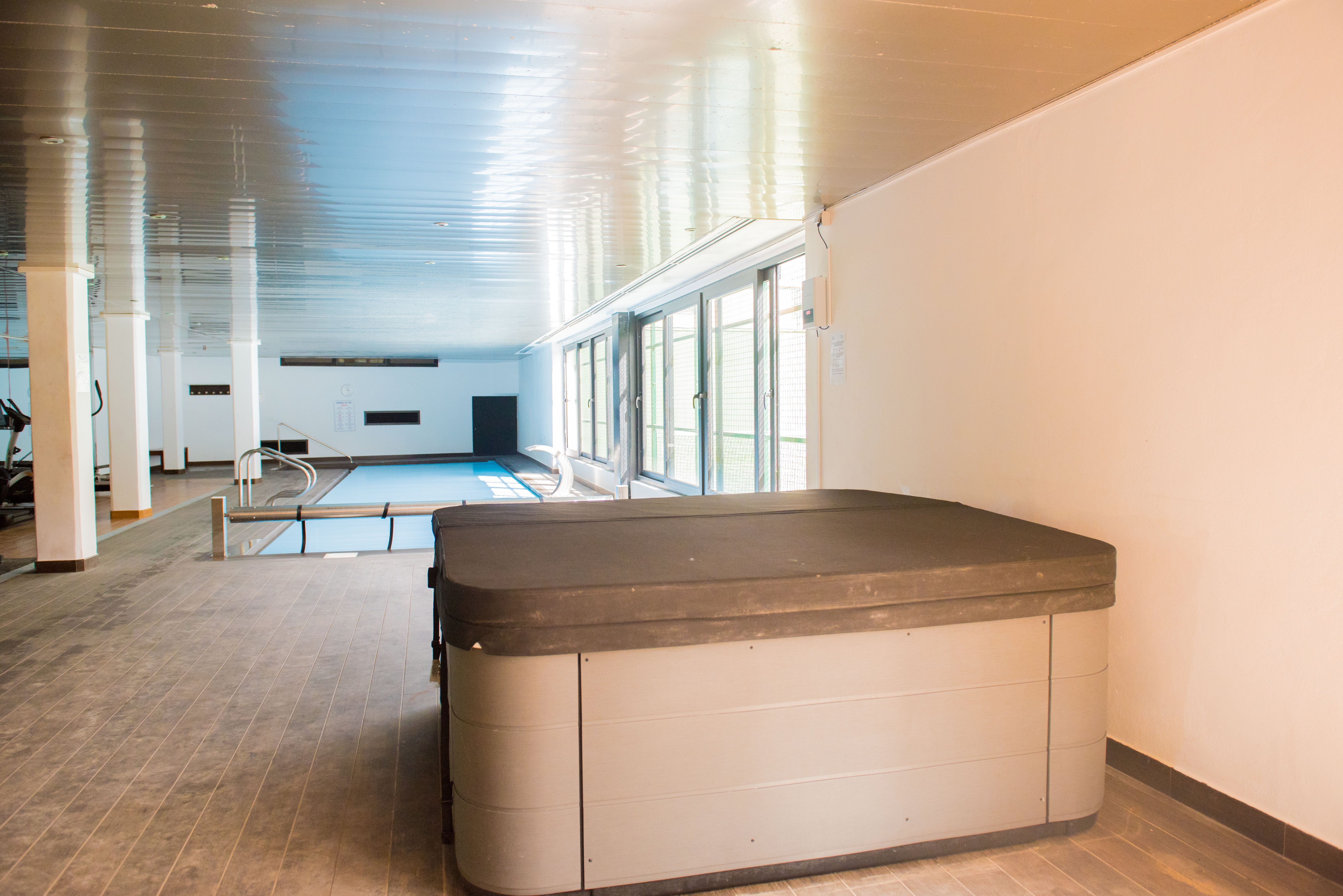 Espace bien-être intérieur comprenant un jacuzzi avec couvercle, une piscine et un coin fitness, bénéficiant de grandes baies vitrées.