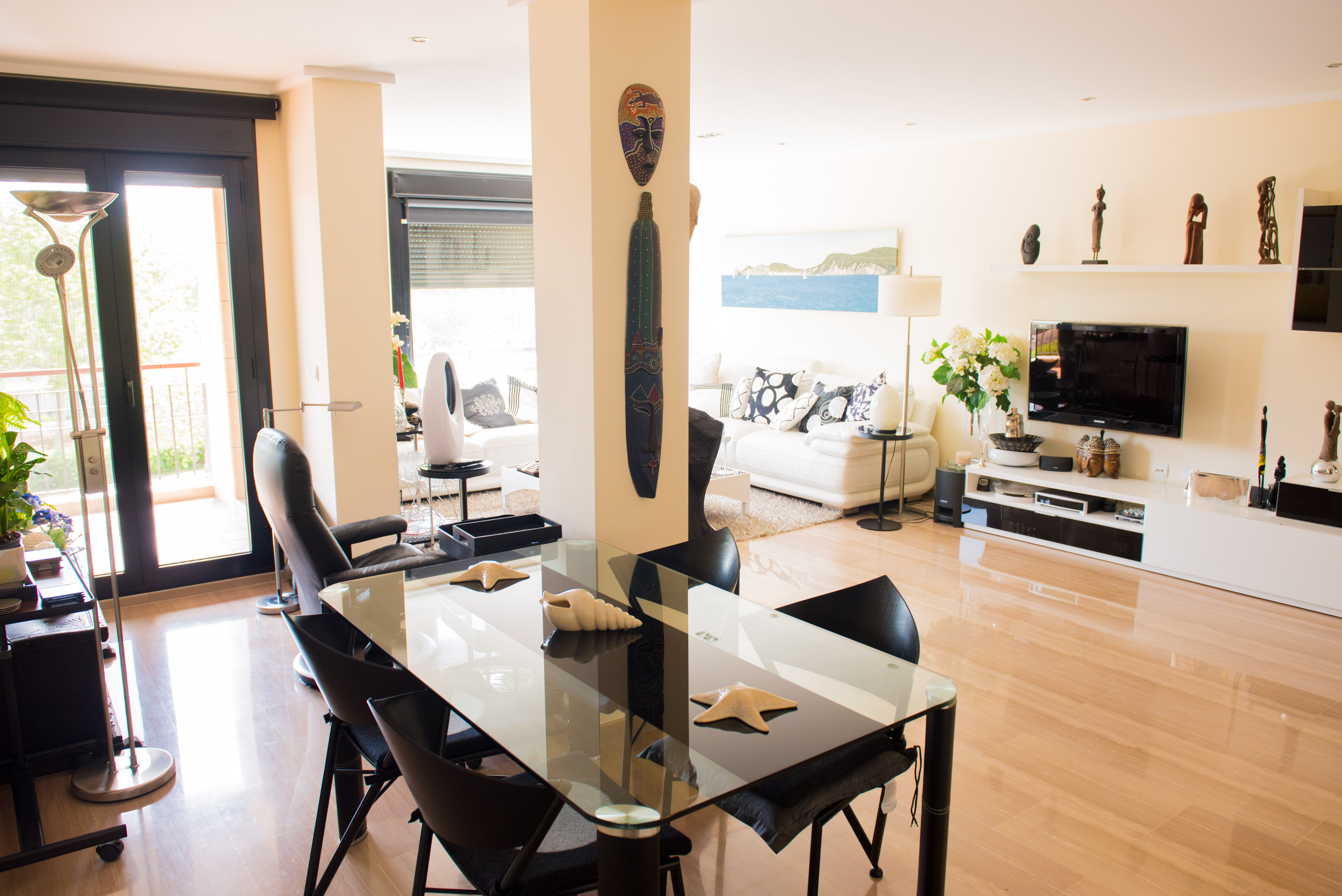 Espace de vie lumineux avec sol en marbre poli, table à manger en verre et accès au balcon. Décoration élégante avec des accents ethniques et éclairage encastré.