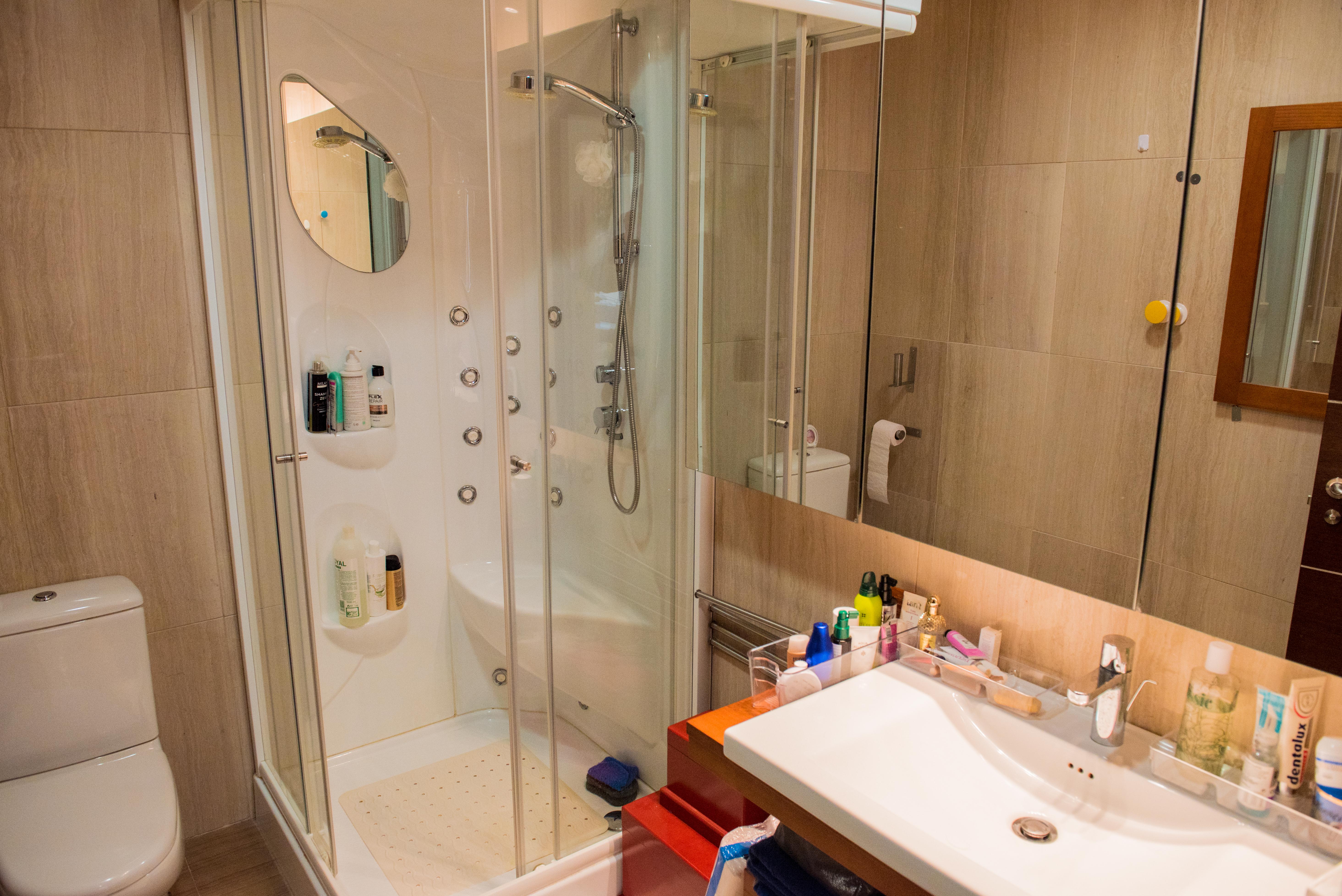 Salle de bain moderne avec cabine de douche d'hydromassage, parois en verre, lavabo blanc design et murs revêtus de carrelage aux tons neutres.