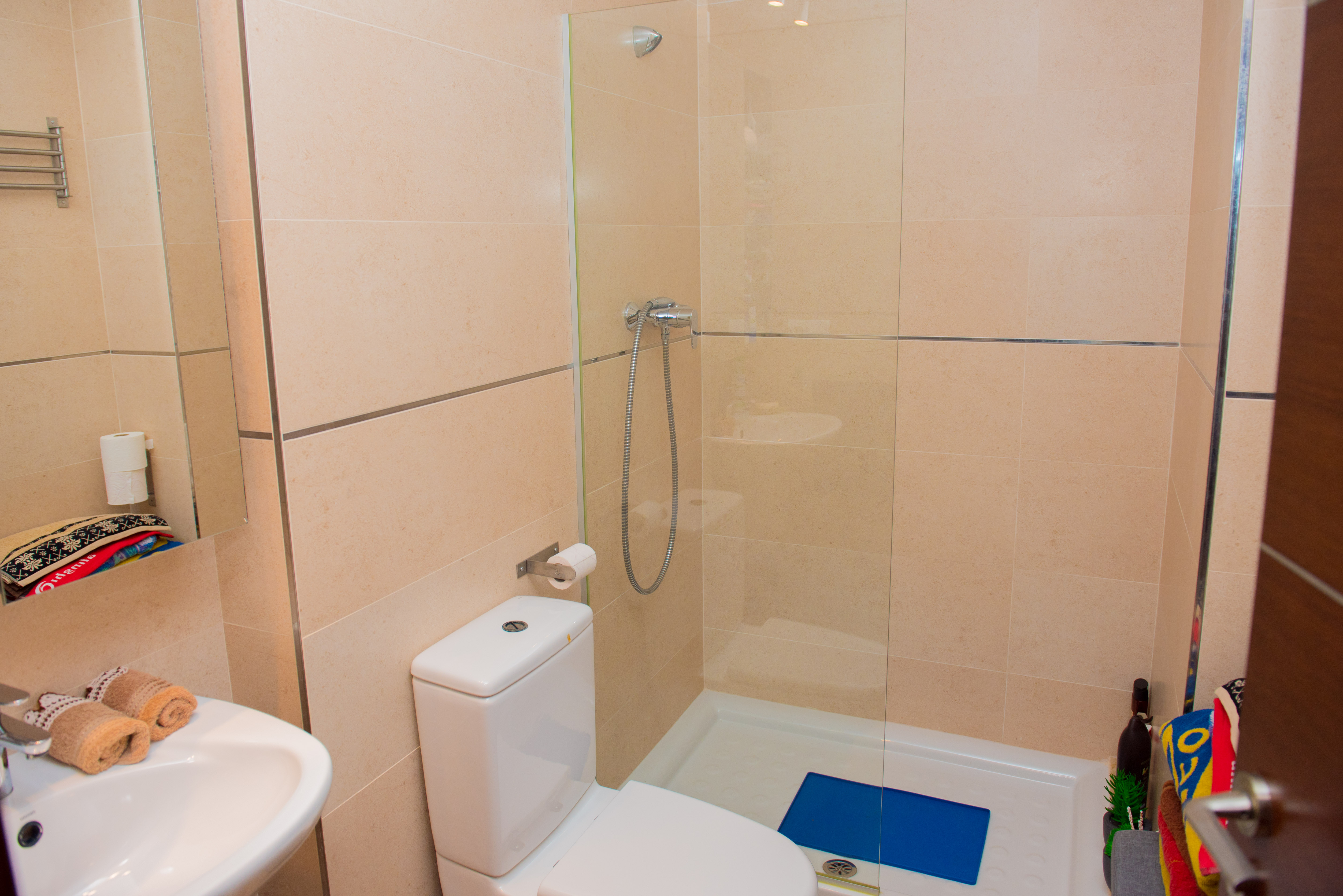 Salle de bain moderne avec douche à l'italienne, paroi en verre, toilettes blanches et carrelage mural beige aux finitions chromées.