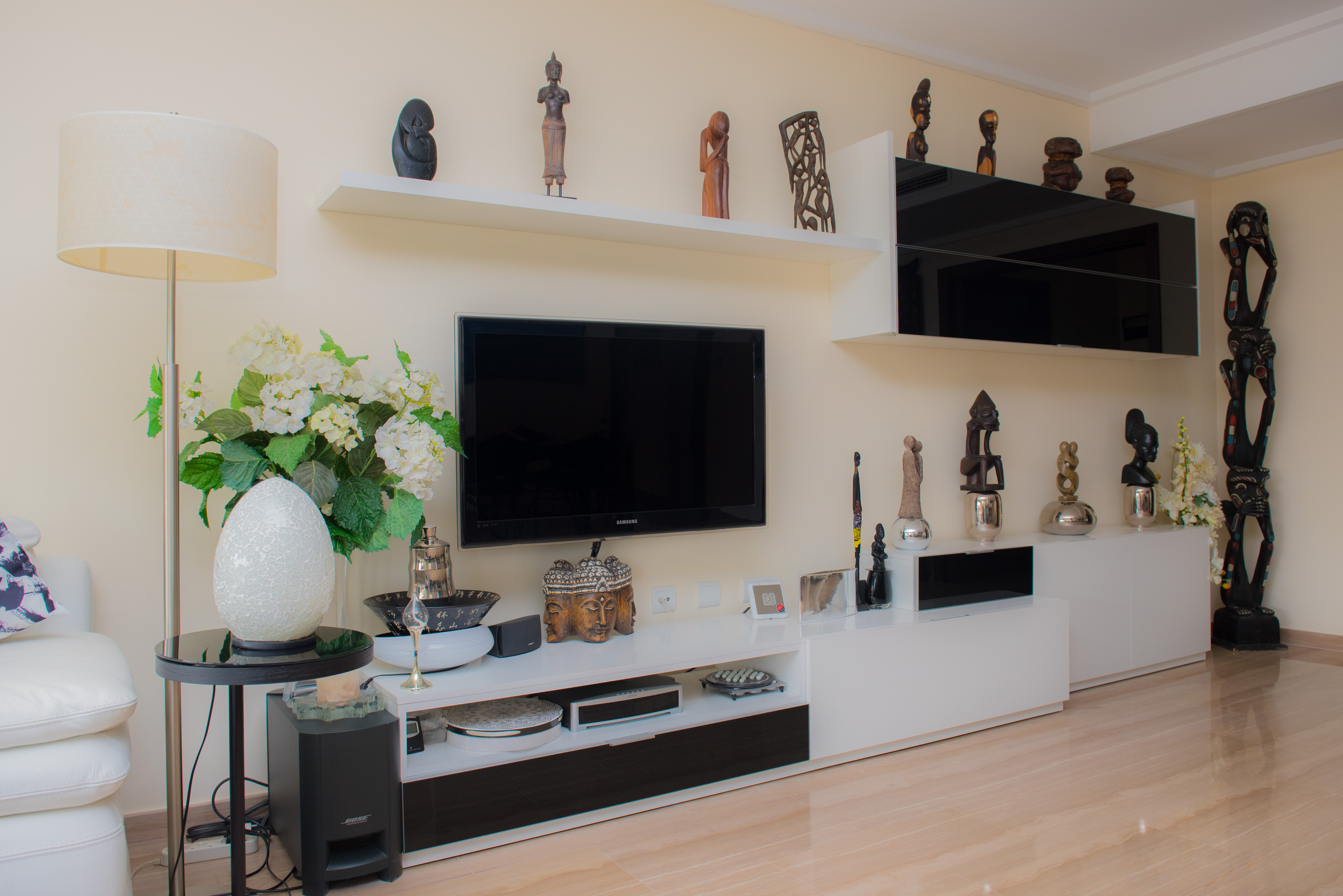 Salon avec un meuble TV moderne noir et blanc, des étagères flottantes présentant diverses sculptures et un sol en grès cérame clair. Une lampe sur pied et des éléments décoratifs enrichissent l'espace. Salon avec un meuble TV moderne noir et blanc, des étagères flottantes présentant diverses sculptures et un sol en grès cérame clair. Une lampe sur pied et des éléments décoratifs enrichissent l'espace.