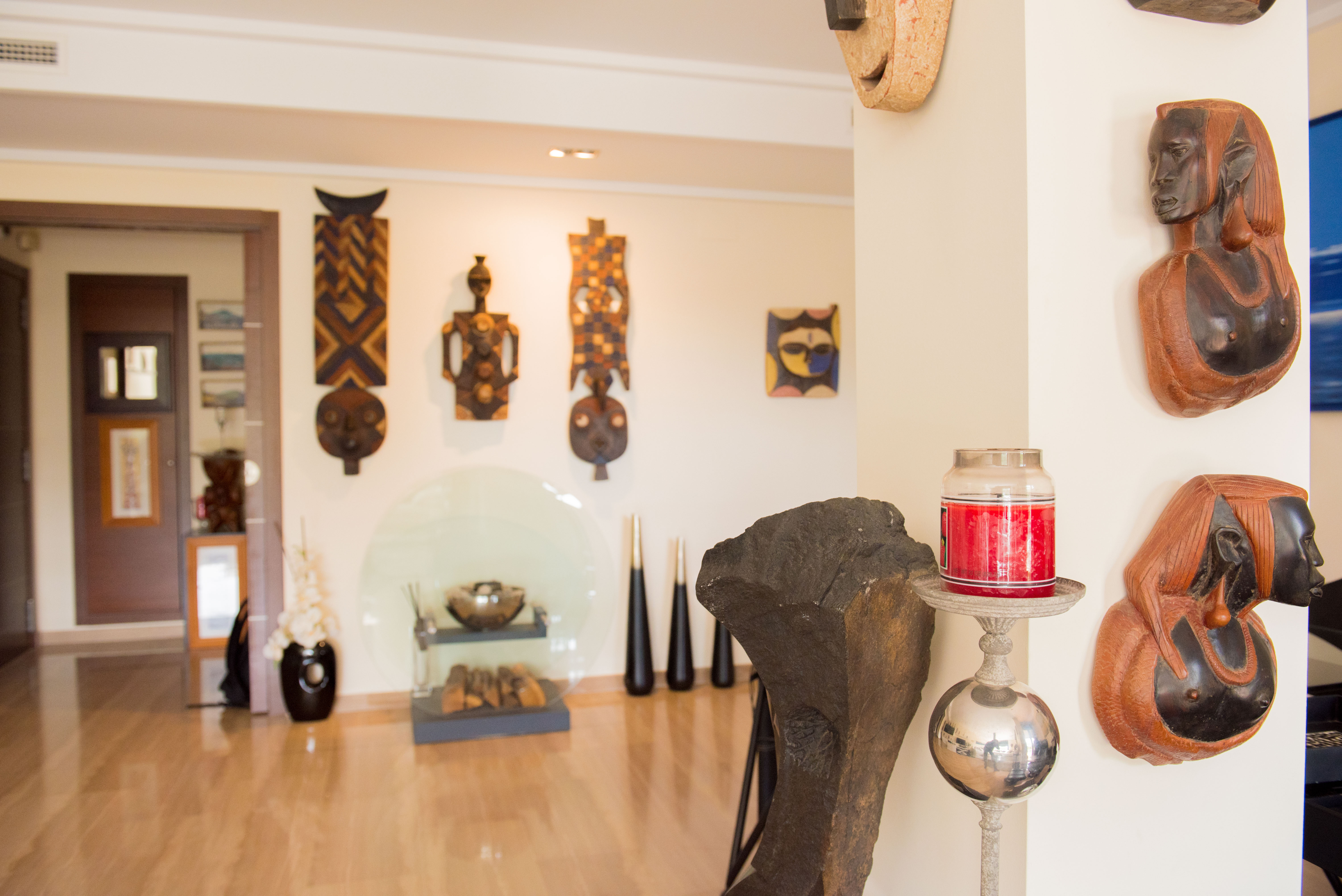 Un intérieur artistique présentant une collection soignée de masques et bustes en bois sculpté sur des murs clairs, complété par un parquet poli et des accents décoratifs modernes. Un intérieur artistique présentant une collection soignée de masques et bustes en bois sculpté sur des murs clairs, complété par un parquet poli et des accents décoratifs modernes.
