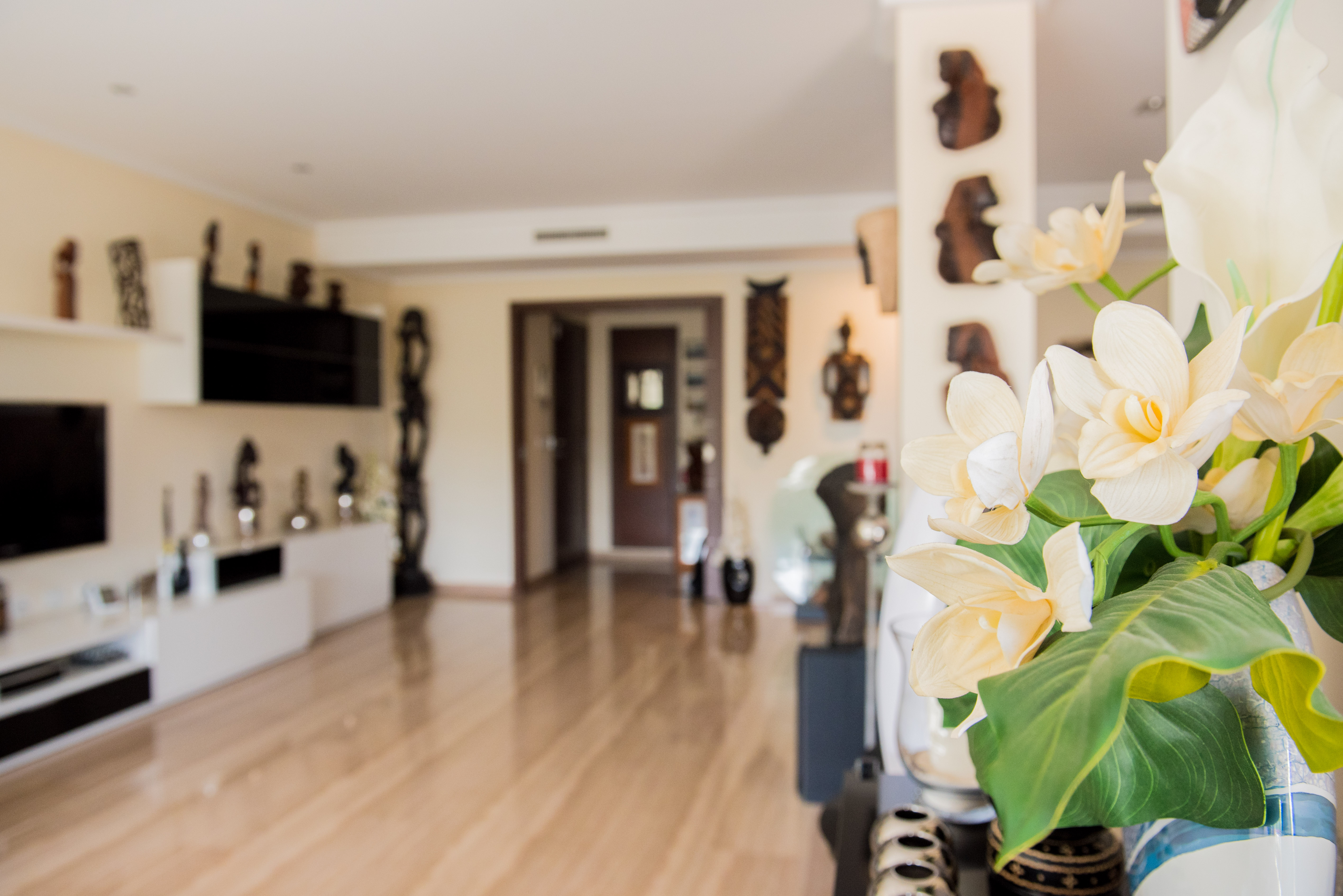 Vase au premier plan avec d'élégantes fleurs artificielles blanches et jaunes. Intérieur lumineux avec parquet clair, menant à un salon moderne agrémenté d'art mural décoratif. Vase au premier plan avec d'élégantes fleurs artificielles blanches et jaunes. Intérieur lumineux avec parquet clair, menant à un salon moderne agrémenté d'art mural décoratif.