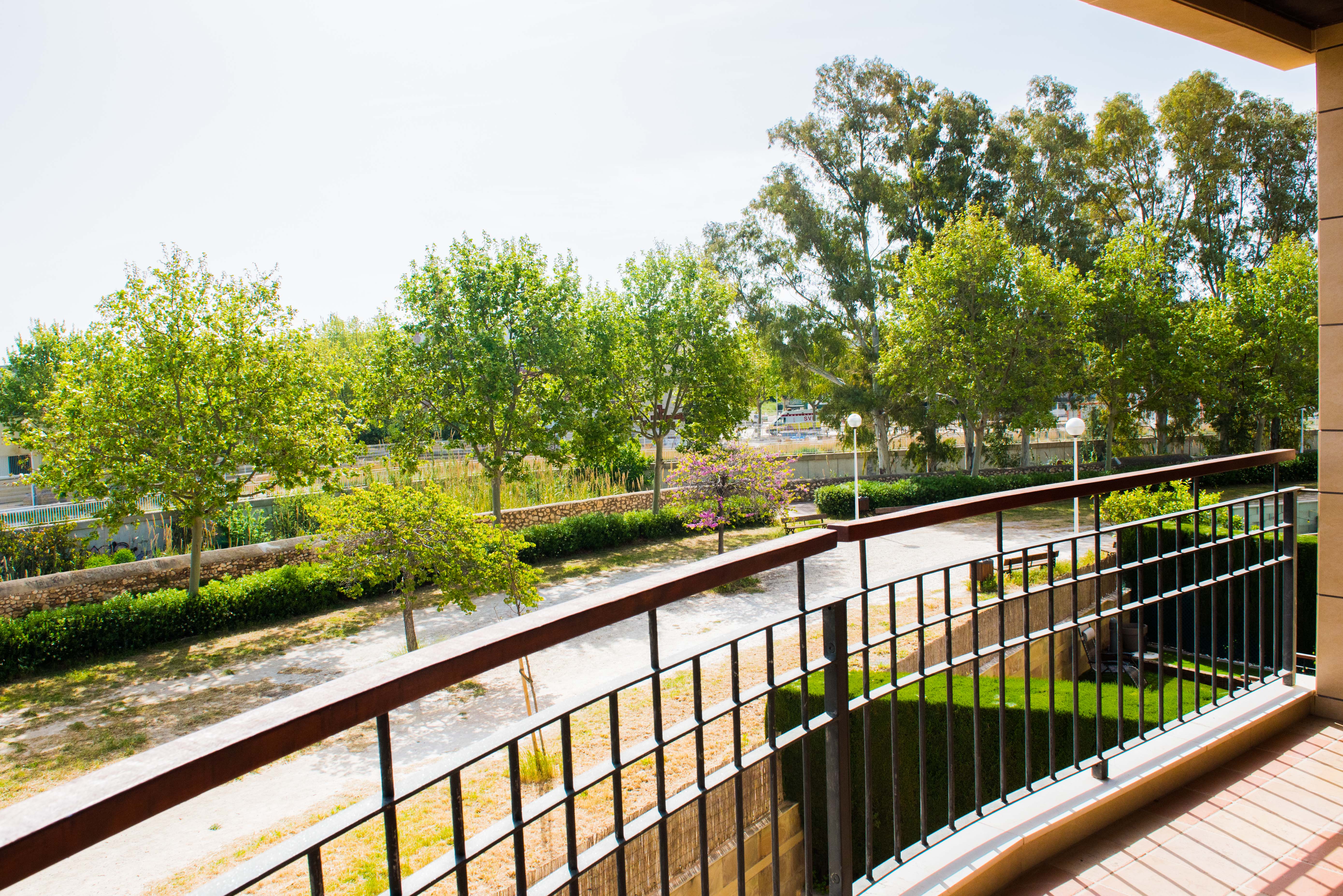 Vue depuis une terrasse privée sur de luxuriants jardins communautaires avec des arbres matures, un sentier sinueux et un mur en pierre, sous un ciel lumineux. La balustrade est métallique et le sol carrelé. Vue depuis une terrasse privée sur de luxuriants jardins communautaires avec des arbres matures, un sentier sinueux et un mur en pierre, sous un ciel lumineux. La balustrade est métallique et le sol carrelé.