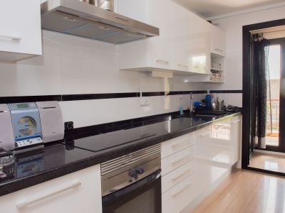 Cuisine moderne avec armoires blanches brillantes, comptoir en granit foncé, électroménagers intégrés et accès direct au balcon.