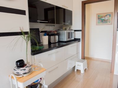 Cuisine moderne avec des meubles bas blancs, un plan de travail noir et des éléments hauts sombres. Équipée d'un micro-ondes, elle s'ouvre sur une pièce adjacente avec un sol carrelé clair.