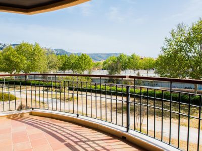 Grande terrasse incurvée avec sol en carreaux de terre cuite et balustrade métallique, offrant des vues sur la verdure et les montagnes lointaines.