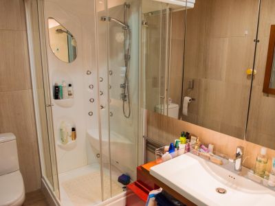 Salle de bain moderne avec cabine de douche vitrée, équipée de jets hydromassants et d'un lavabo intégré. Les murs sont revêtus de carrelage beige.