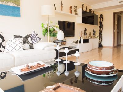 Salon avec canapé blanc, coussins graphiques et table basse noire brillante ornée de détails décoratifs. Meuble TV avec étagères et sculptures africaines.