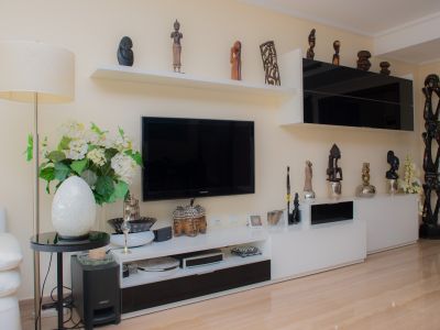 Salon avec un meuble TV moderne noir et blanc, des étagères flottantes présentant diverses sculptures et un sol en grès cérame clair. Une lampe sur pied et des éléments décoratifs enrichissent l'espace.