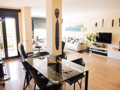 Vaste salon-salle à manger contemporain avec parquet clair. Il présente une table en verre avec des chaises noires, un canapé blanc et un accès à une terrasse via des portes vitrées sombres.