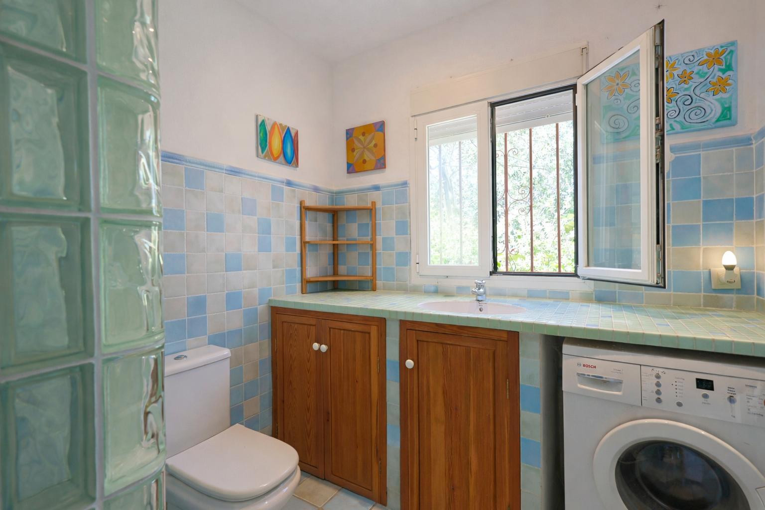 Salle de bain fonctionnelle avec carrelage bleu, plan de travail carrelé avec lavabo intégré, meubles en bois et coin buanderie lumineux.