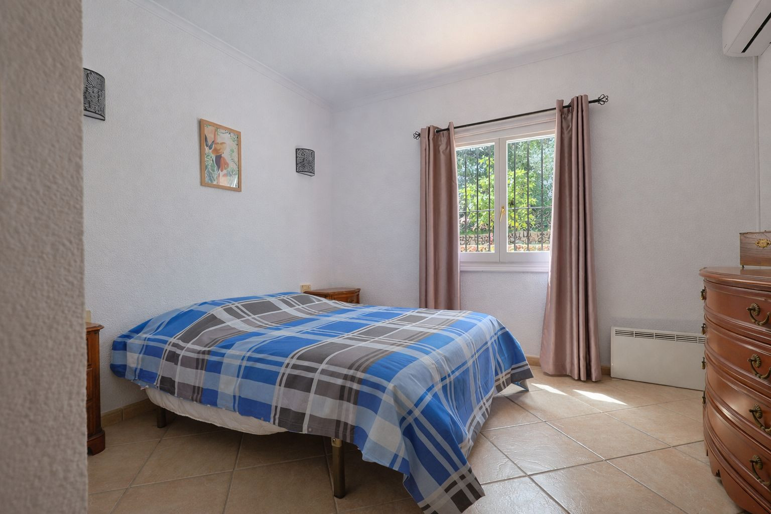 Chambre lumineuse avec sol en grès, mobilier en bois classique et vue sur le jardin. Équipée de la climatisation et d'un chauffage électrique mural.
