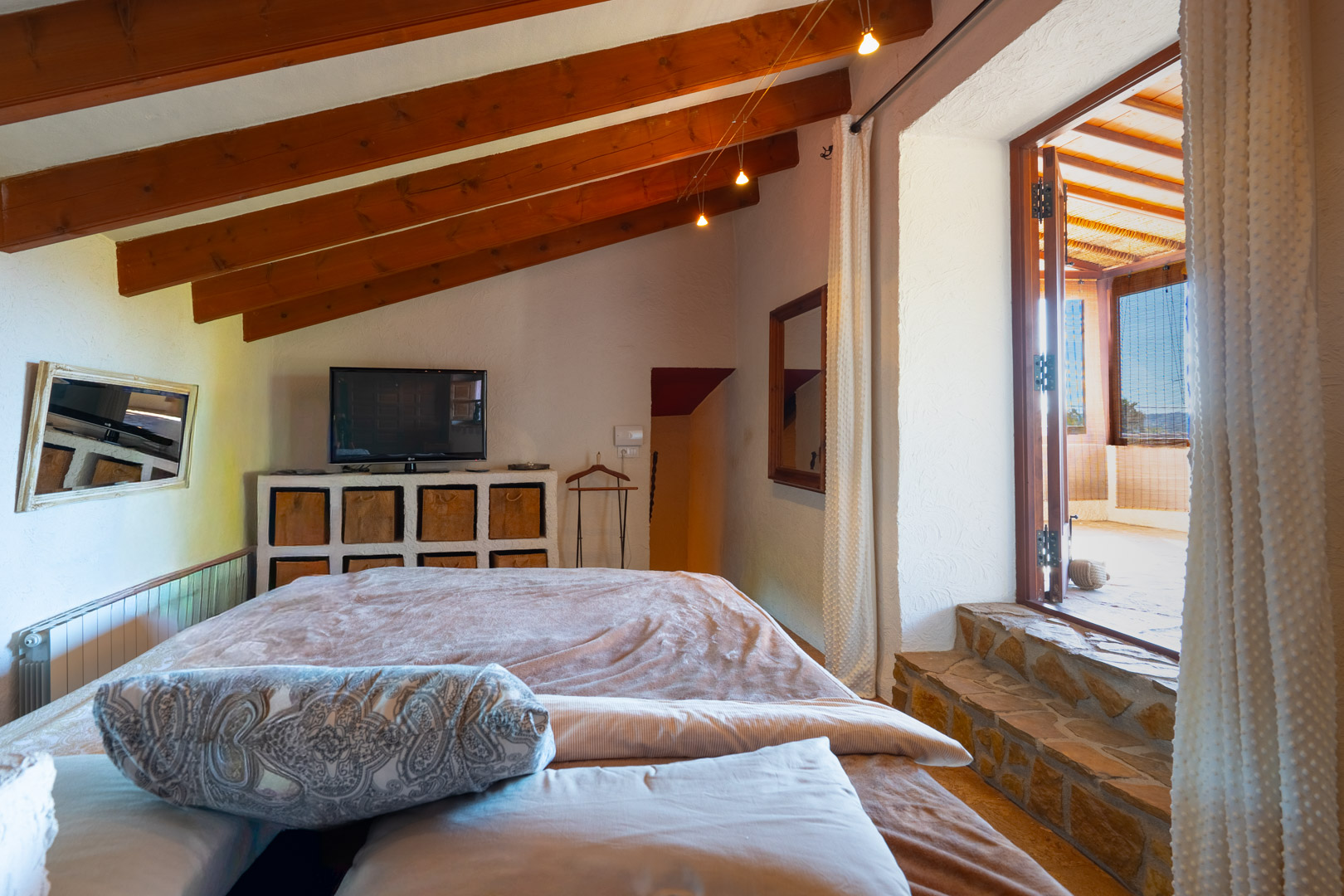 Chambre avec poutres en bois apparentes et marches en pierre naturelle offrant un accès direct à la naya vitrée.