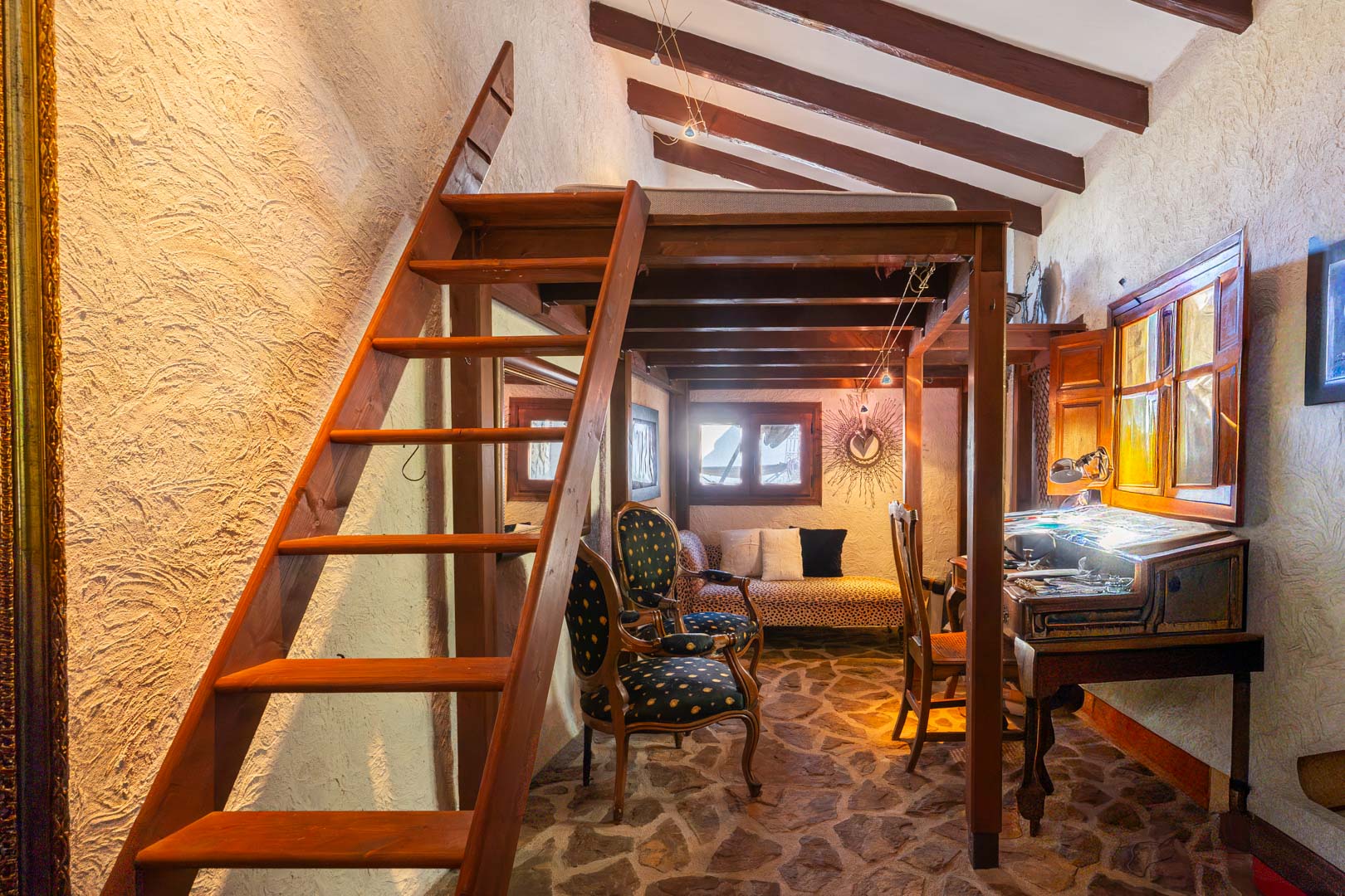 Chambre rustique avec mezzanine en bois, poutres apparentes et sol en pierre naturelle. L'espace comprend un coin bureau ancien et du mobilier de style classique.