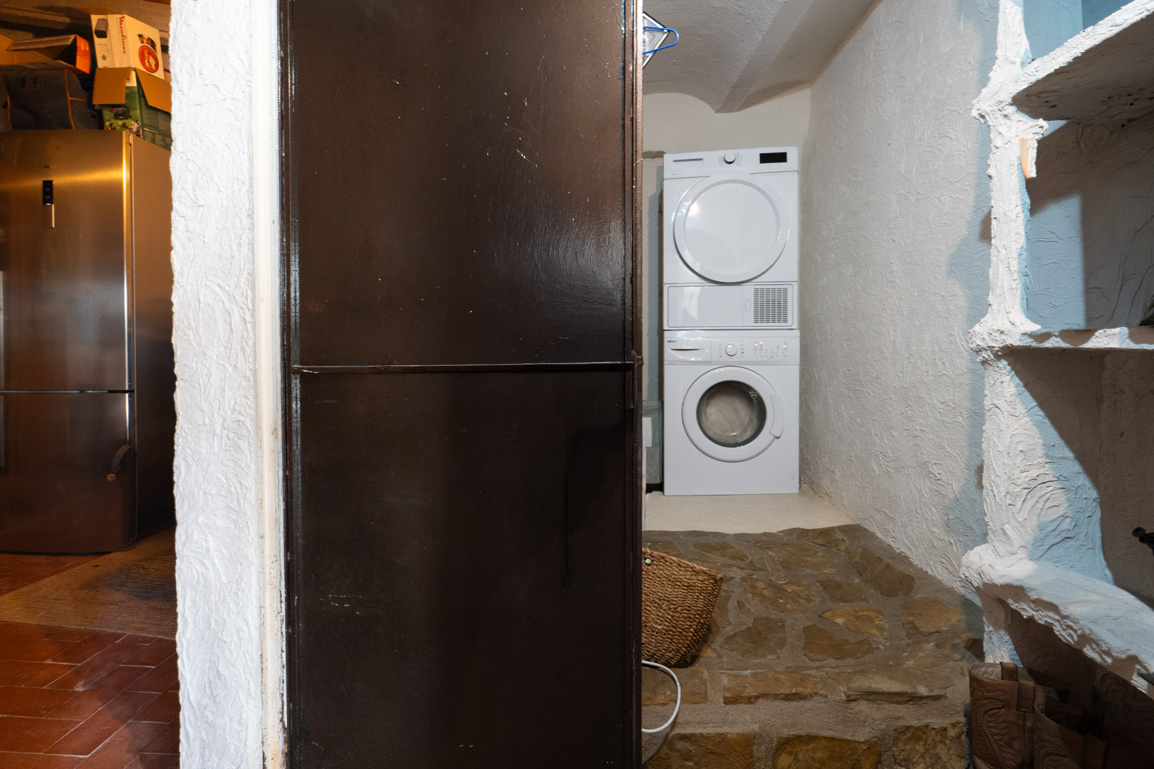Espace buanderie fonctionnel comprenant un lave-linge et un sèche-linge superposés, avec des murs texturés et un sol en pierre naturelle.