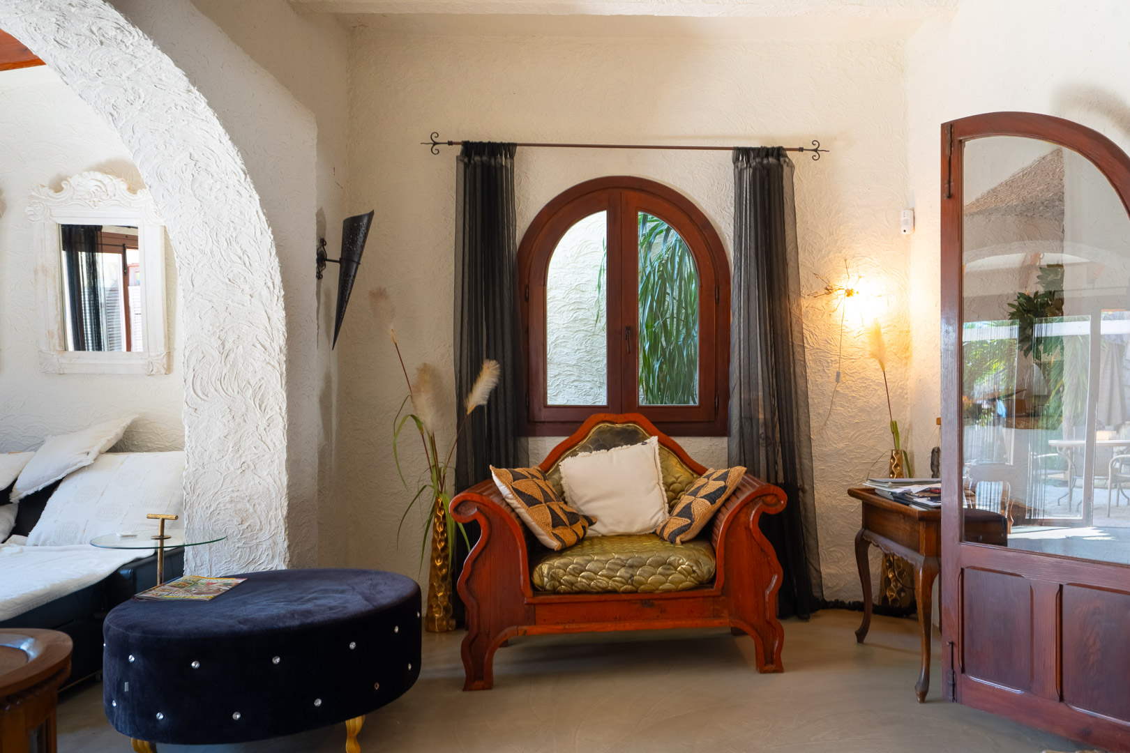Salon avec murs en crépi texturé, un fauteuil en bois sculpté et une fenêtre en plein cintre apportant une lumière naturelle douce.