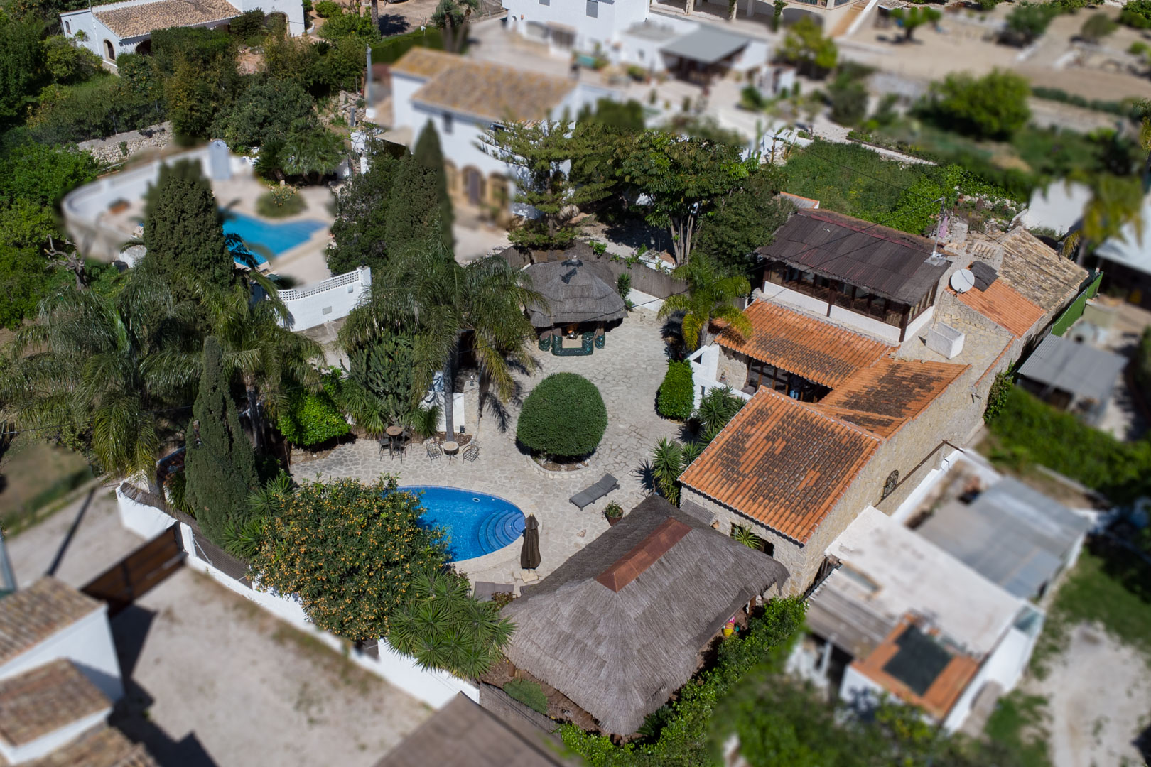 Vue aérienne montrant la piscine ovale, le patio en pierre naturelle et les pergolas balinaises entourées d'une végétation méditerranéenne dense.