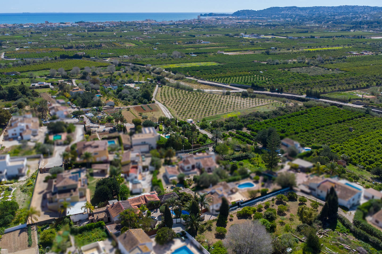 Vue aérienne montrant l'emplacement de la propriété entourée de vergers, avec le littoral méditerranéen et la baie de Jávea à l'horizon.