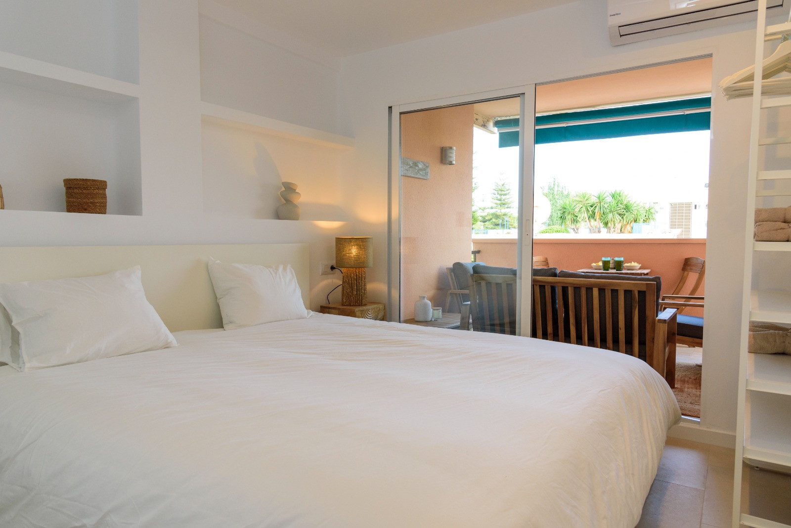 Chambre avec niches murales intégrées et accès direct à une terrasse meublée par des baies vitrées, offrant une transition fluide entre intérieur et extérieur.
