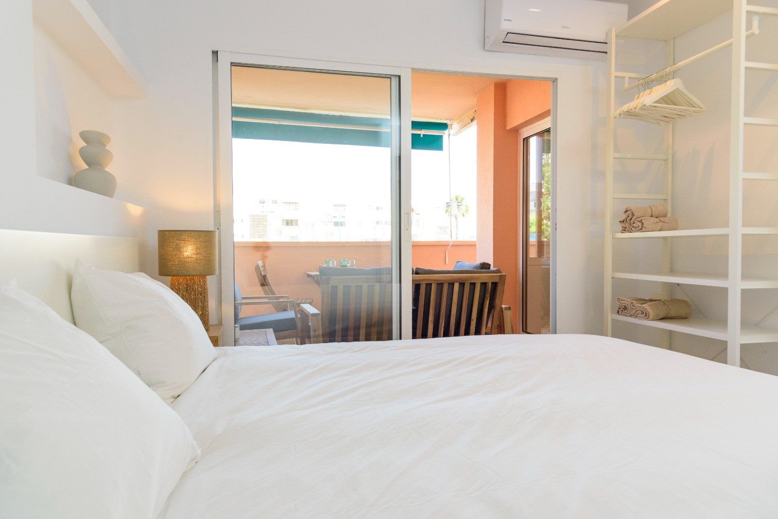 Chambre lumineuse avec accès direct à la terrasse meublée, penderie ouverte au design minimaliste et climatisation individuelle pour un confort optimal.