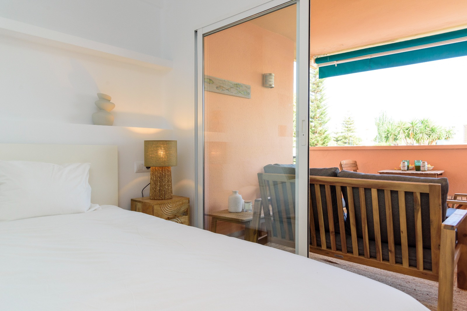 Chambre lumineuse avec accès direct à une terrasse privée meublée en bois. L'espace se distingue par sa lumière naturelle et son design épuré aux tons neutres.