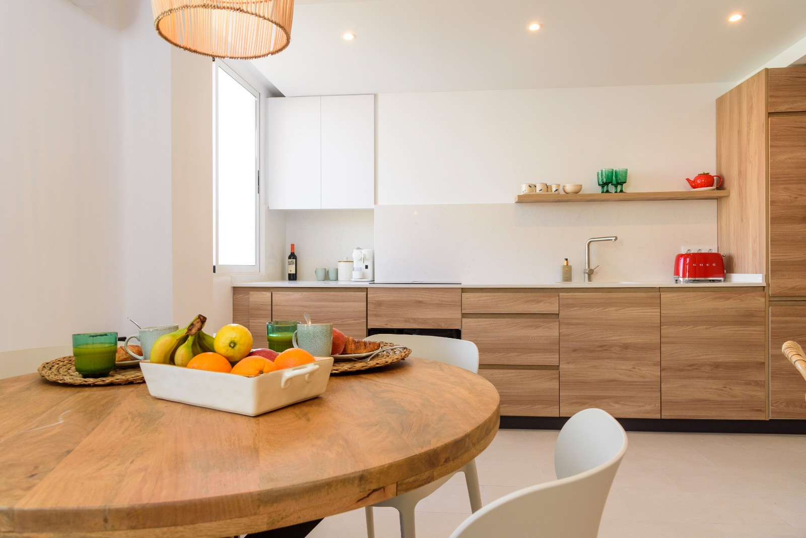 Coin repas avec table ronde en bois et cuisine ouverte aux finitions en chêne, dotée d'un plan de travail blanc et d'un éclairage encastré élégant.