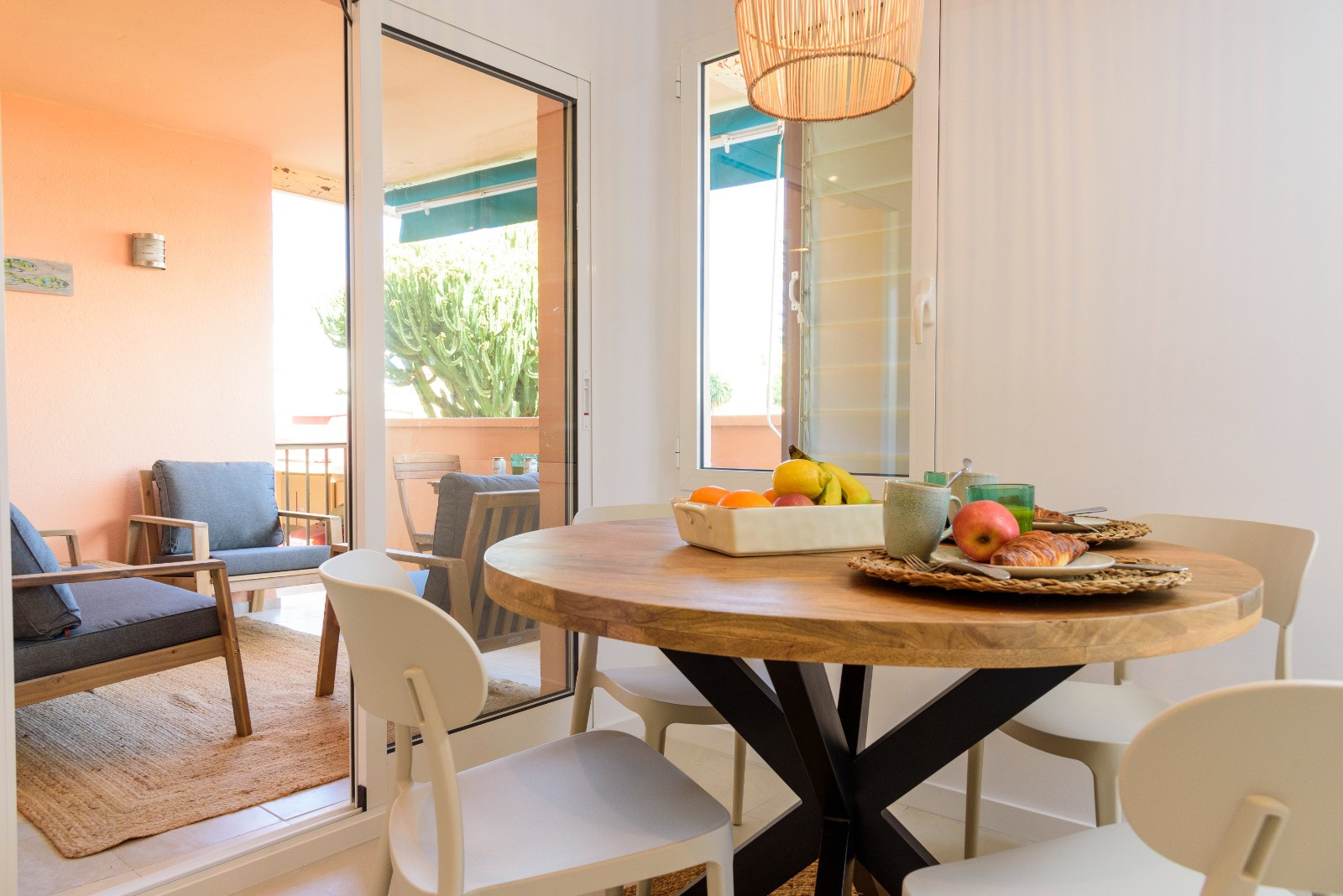 Coin repas lumineux avec table ronde en bois et chaises blanches, s'ouvrant sur une terrasse aménagée grâce à de grandes baies vitrées offrant une belle clarté.