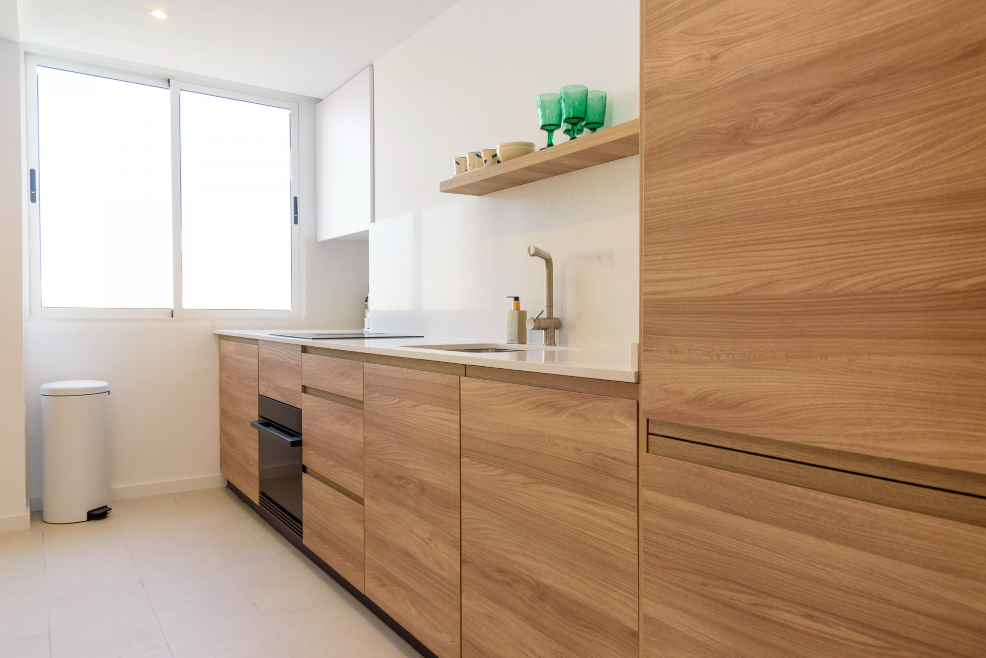 Cuisine moderne avec des meubles en bois clair, un plan de travail blanc et un évier intégré. Une grande fenêtre apporte une lumière naturelle abondante sur les finitions épurées.
