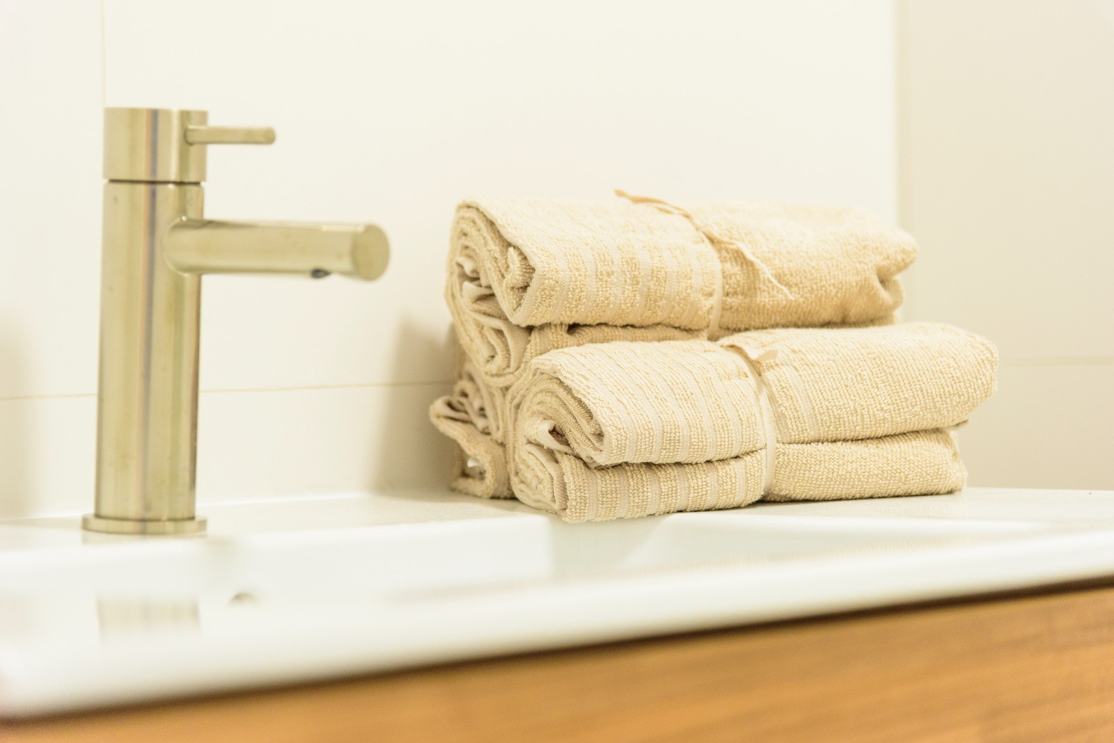 Détail de la salle de bain avec robinetterie en acier brossé, vasque blanche et serviettes en coton beige sur un meuble en bois contemporain.