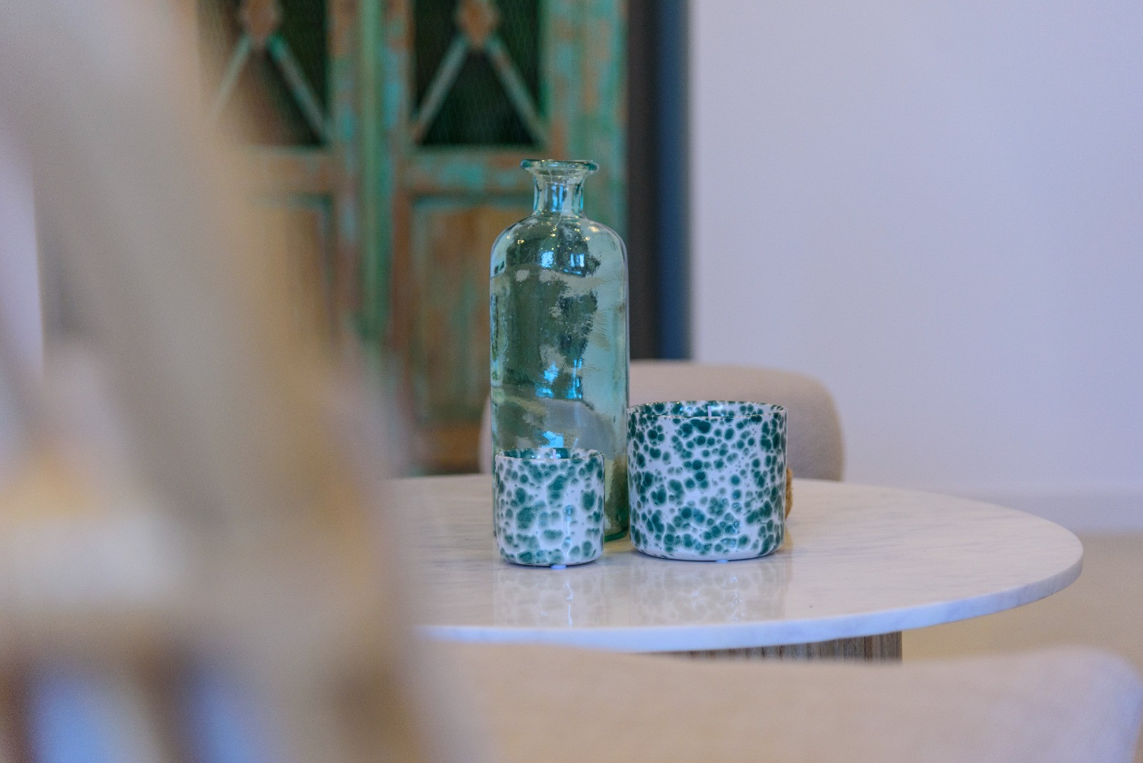 Détail décoratif sur une table en marbre blanc avec une bouteille en verre turquoise et des récipients en céramique sur un fond rustique flou.