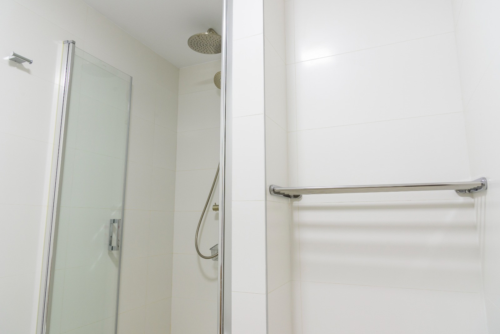 Salle de bain moderne avec douche à l'italienne, paroi en verre et robinetterie chromée avec pommeau effet pluie. Murs revêtus de carreaux blancs et porte-serviettes intégré.