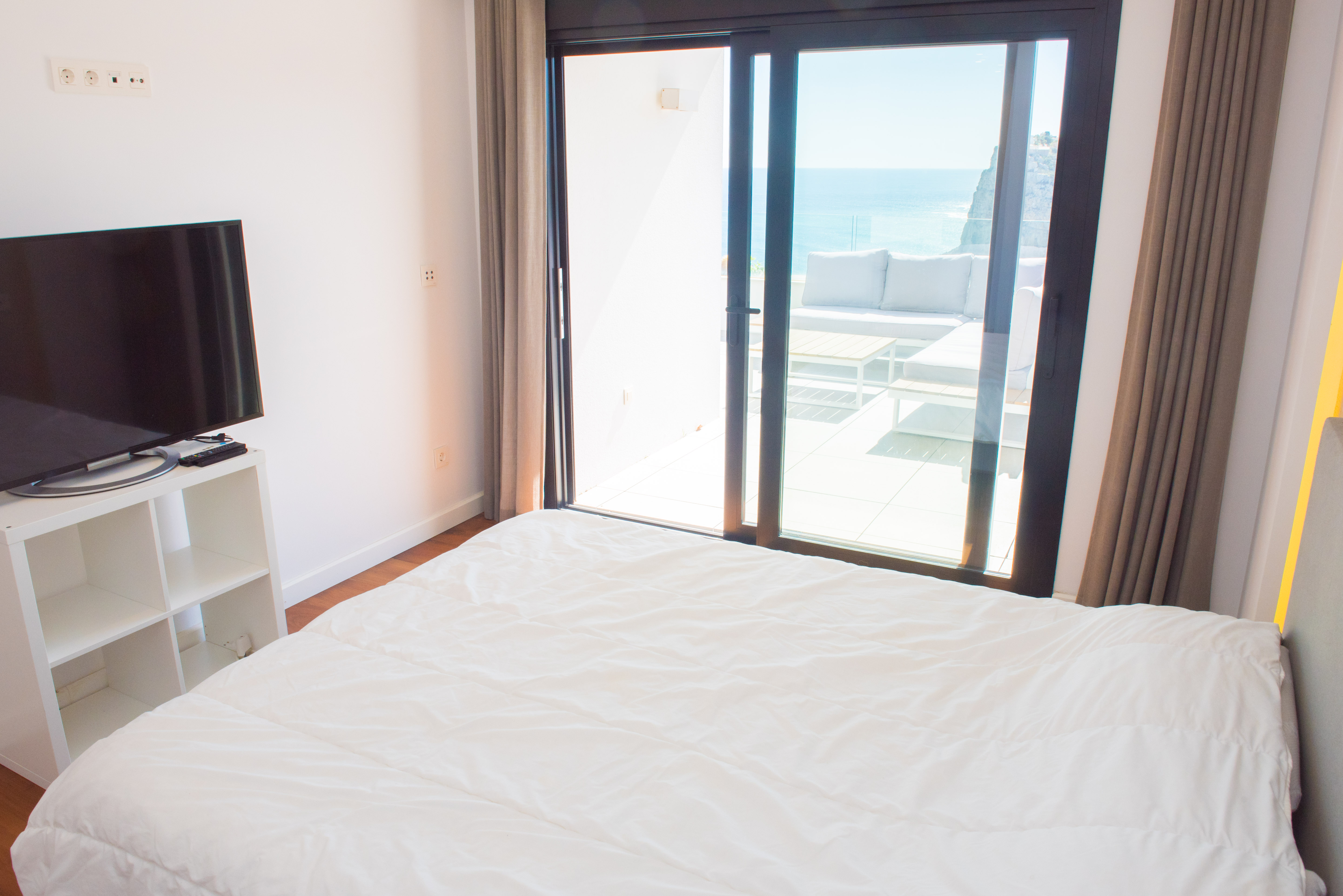 Chambre lumineuse avec accès direct à une terrasse privée équipée de mobilier de jardin, offrant une vue panoramique sur la mer et les falaises.