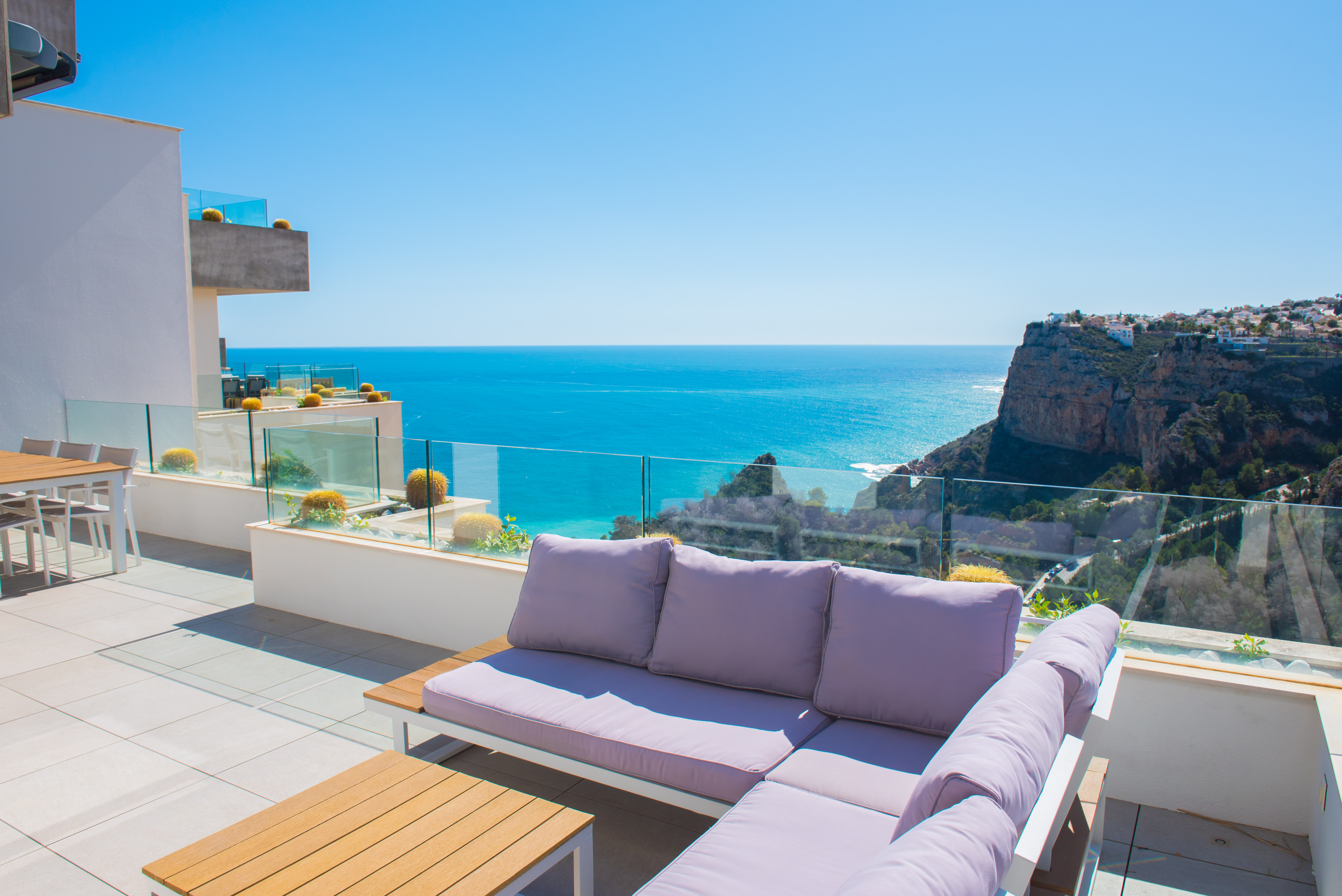 Terrasse privée avec canapé d'angle, garde-corps en verre et vue panoramique sur la mer Méditerranée et les falaises environnantes.
