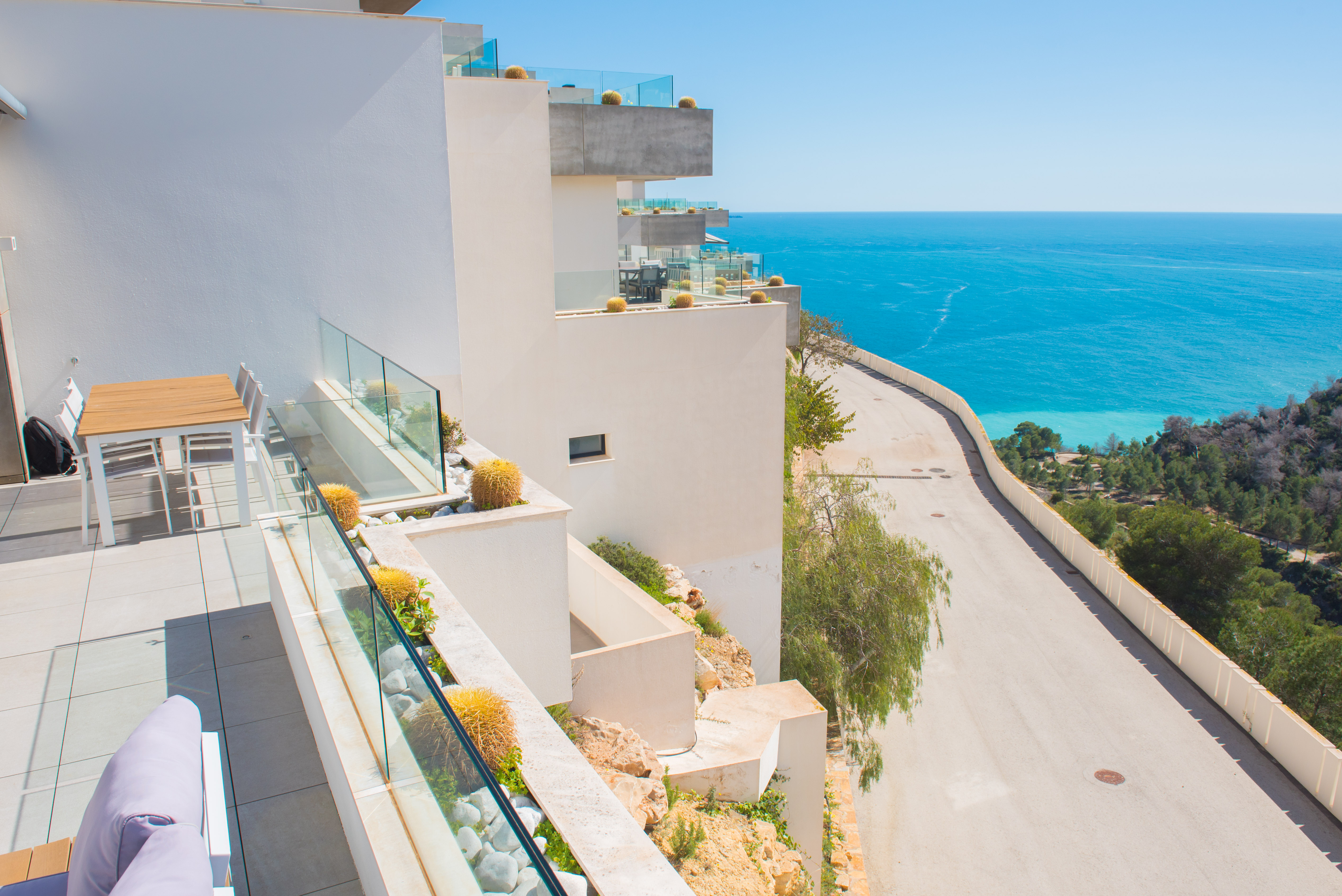 Terrasse privée avec garde-corps en verre et jardinières intégrées de cactus, offrant une vue panoramique sur la mer Méditerranée et la côte.