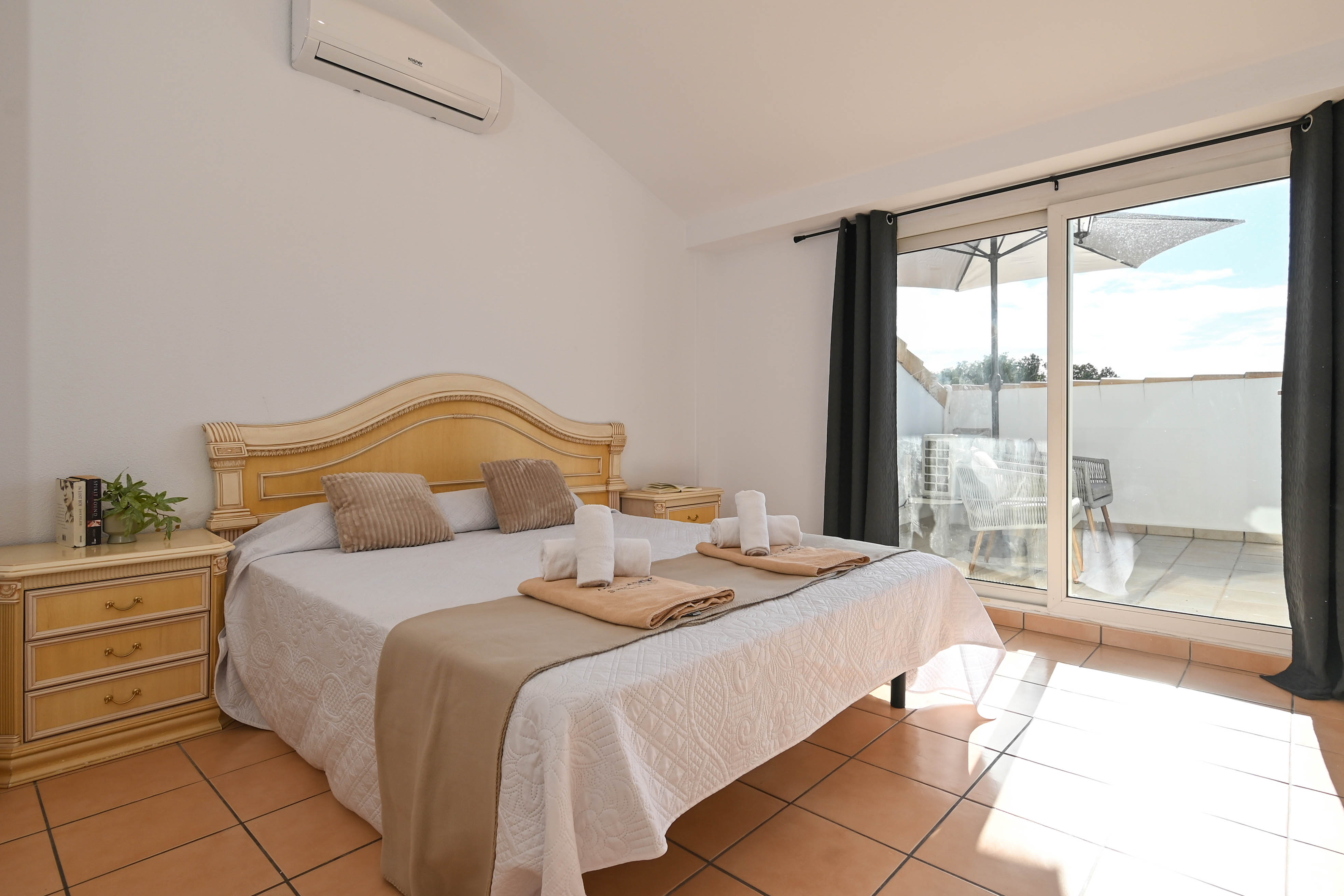 Chambre avec plafonds mansardés, climatisation et accès terrasse. Elle dispose d'un sol en terre cuite et d'un mobilier en bois de style classique.