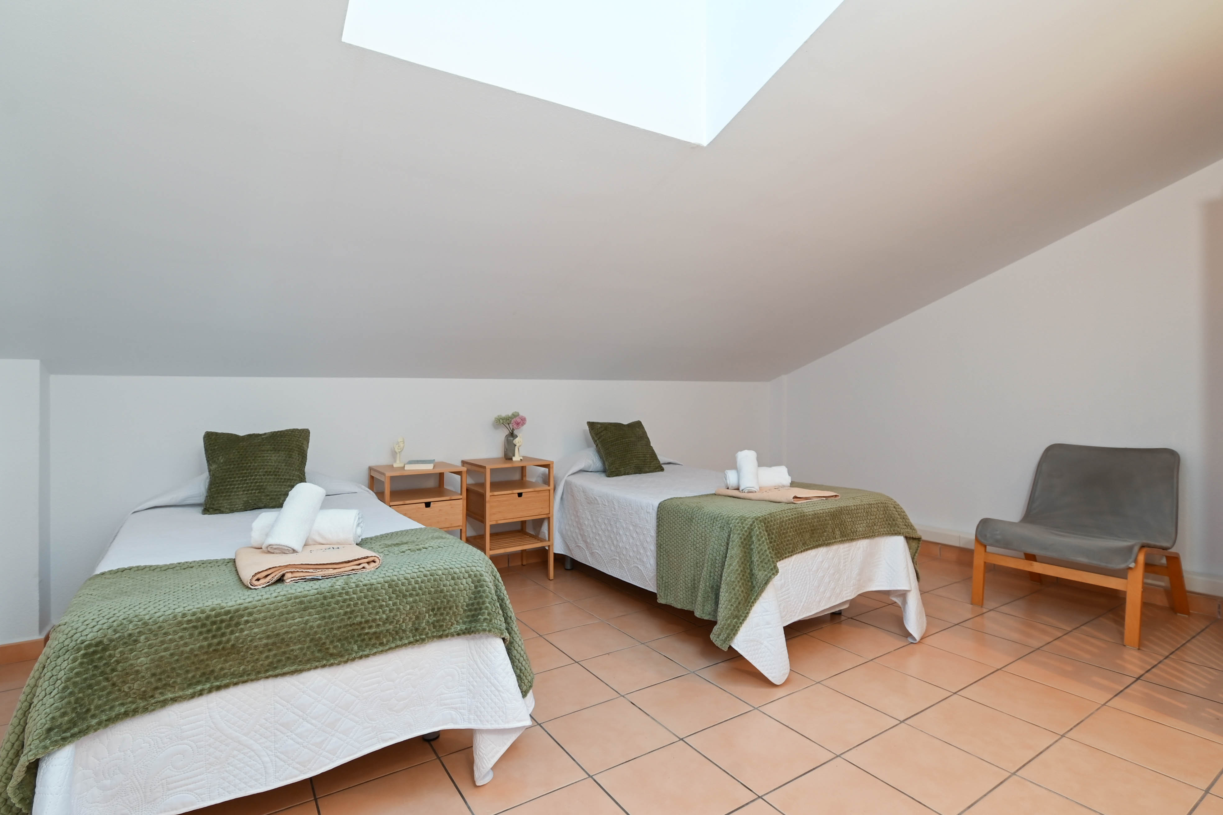 Chambre mansardée avec lits jumeaux, sol en terre cuite et un puits de lumière apportant une clarté naturelle sous le plafond incliné.