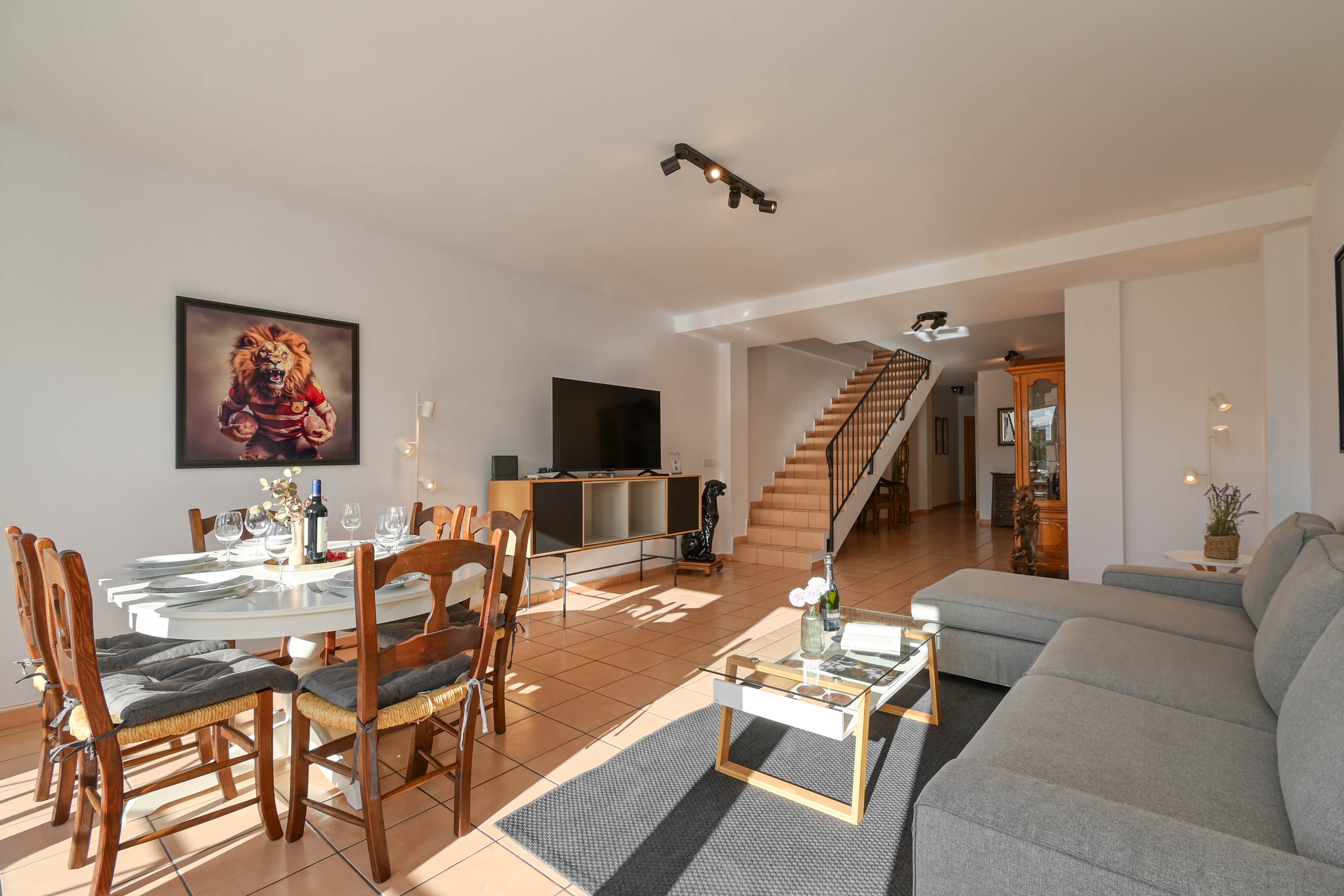 Espace de vie ouvert comprenant un salon avec canapé d'angle, un coin repas et un escalier intérieur sur un sol en carrelage traditionnel.