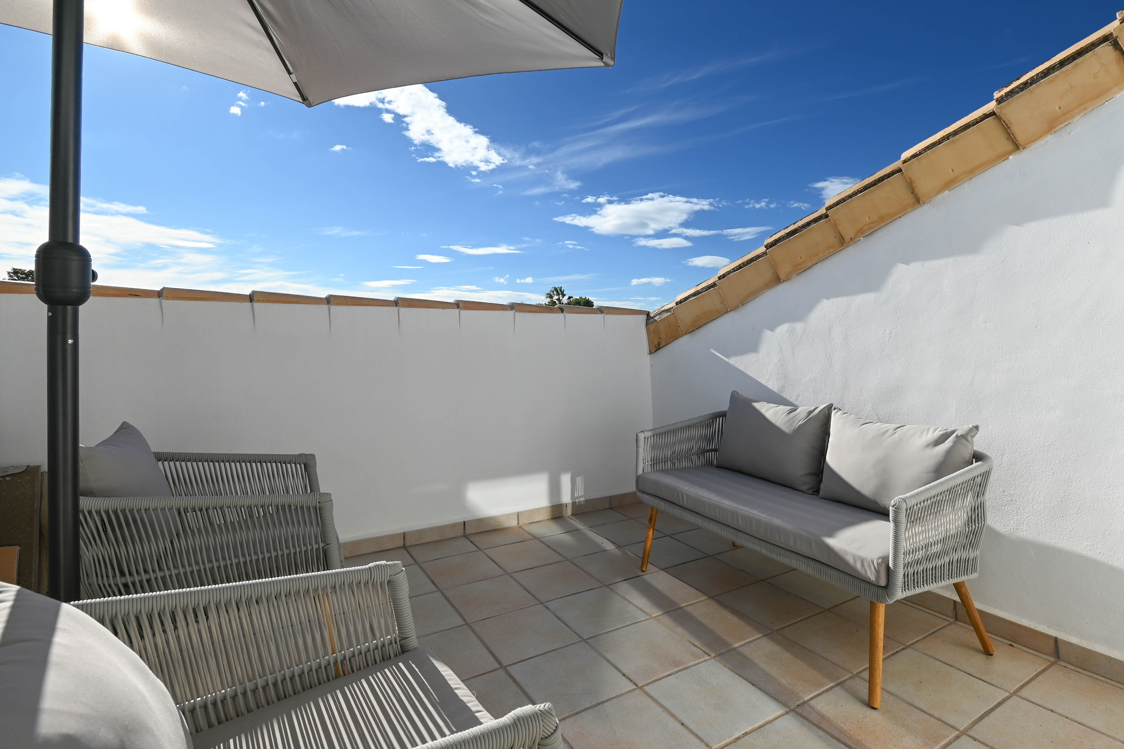 Terrasse privée sur le toit avec mobilier de jardin en corde tressée grise, sol carrelé et parasol, sous le ciel bleu de la Costa Blanca.