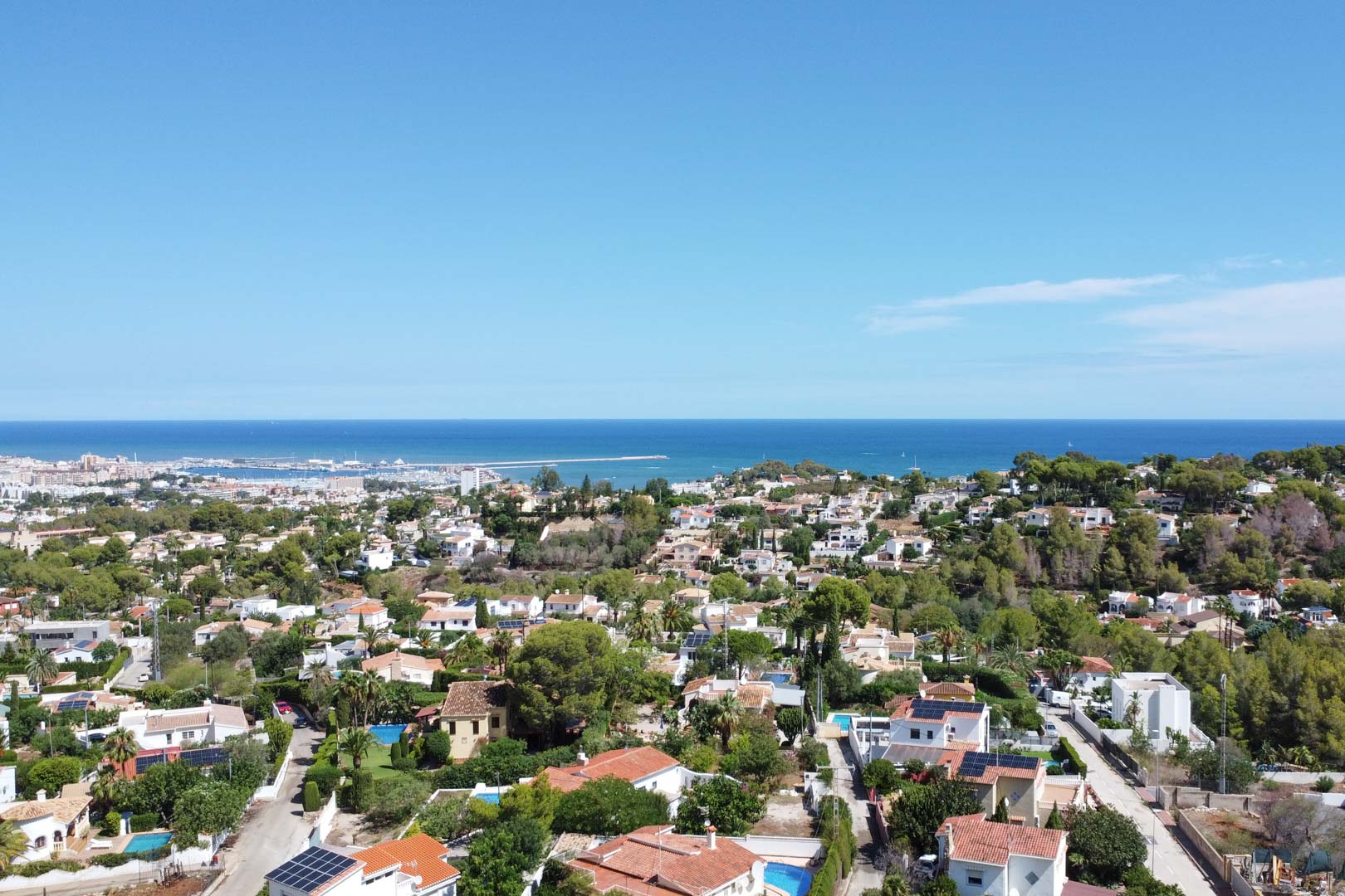 Vue aérienne panoramique du quartier résidentiel de Dénia, offrant une perspective sur la mer Méditerranée, le port et des villas entourées de végétation locale.