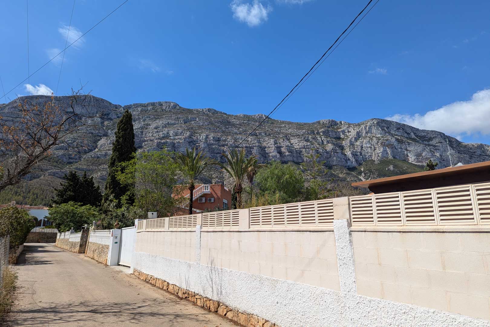 Vue extérieure depuis la rue montrant le mur d'enceinte de la parcelle avec le massif du Montgó en arrière-plan sous un ciel dégagé.