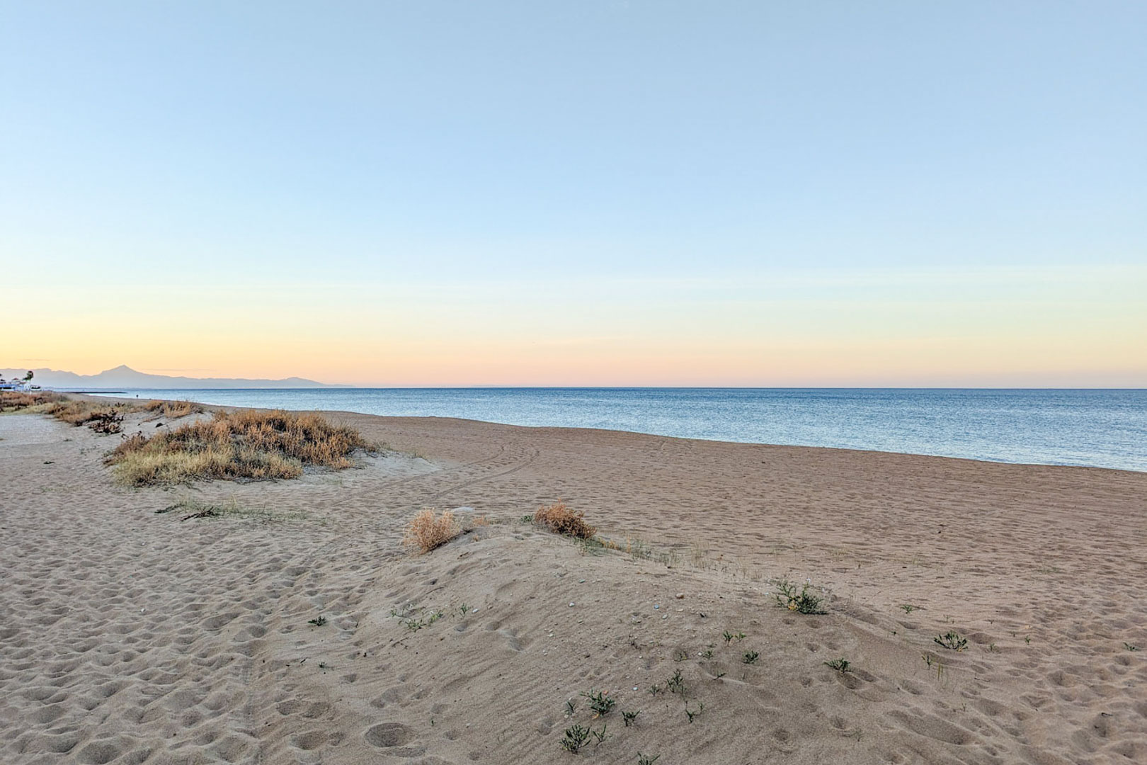 Plage de sable fin avec dunes naturelles et végétation locale à proximité de la propriété. Vue sur la mer Méditerranée et les montagnes lointaines au crépuscule.