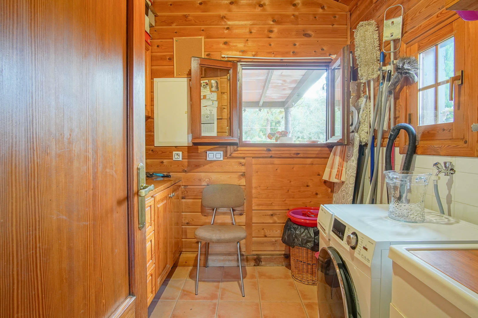 Buanderie fonctionnelle avec murs en pin finlandais, équipée d'un lave-linge, de rangements et d'une fenêtre offrant une vue sur l'extérieur.