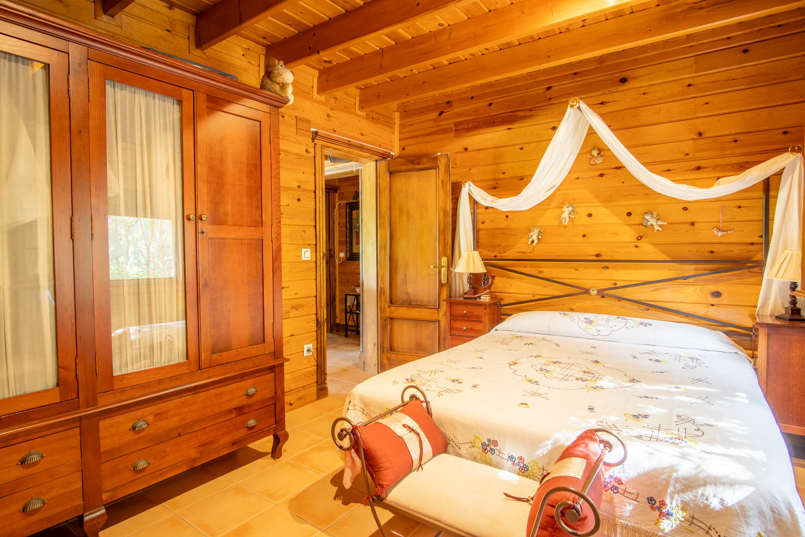 Chambre rustique avec murs et plafonds en pin finlandais, armoire en bois massif et lit double orné d'un baldaquin décoratif et d'une tête de lit en fer forgé.