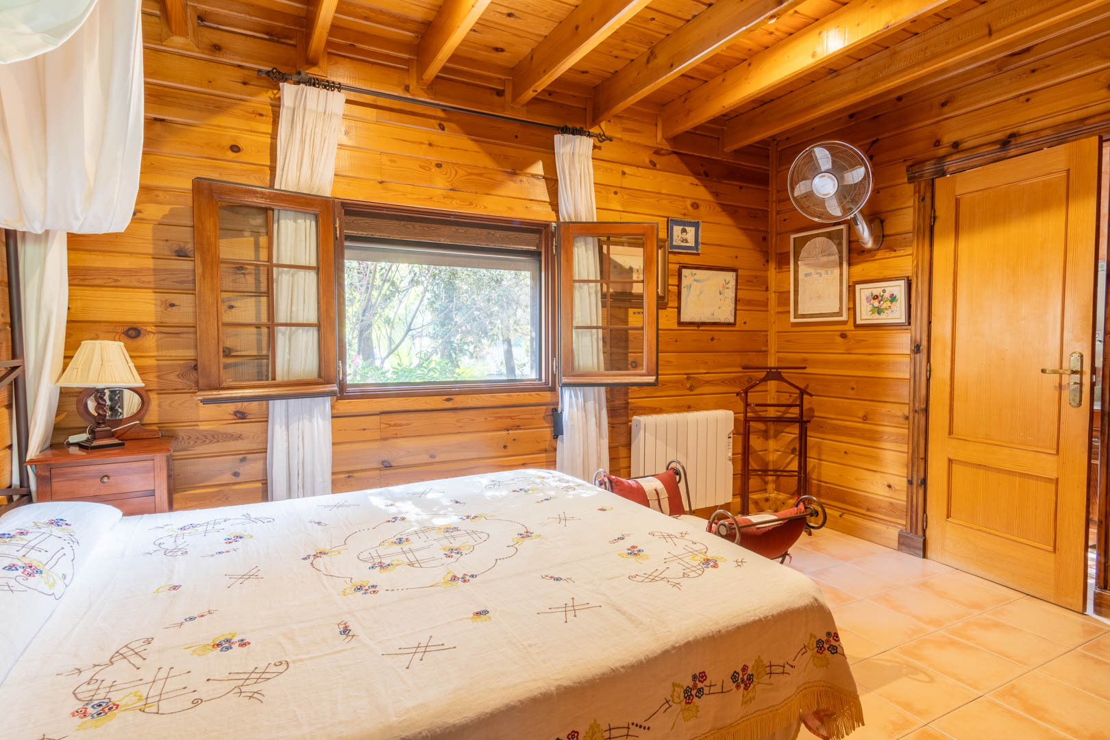 Chambre rustique entièrement revêtue de pin finlandais, avec plafond à poutres apparentes, sol en terre cuite et fenêtre à volets en bois offrant une lumière naturelle.