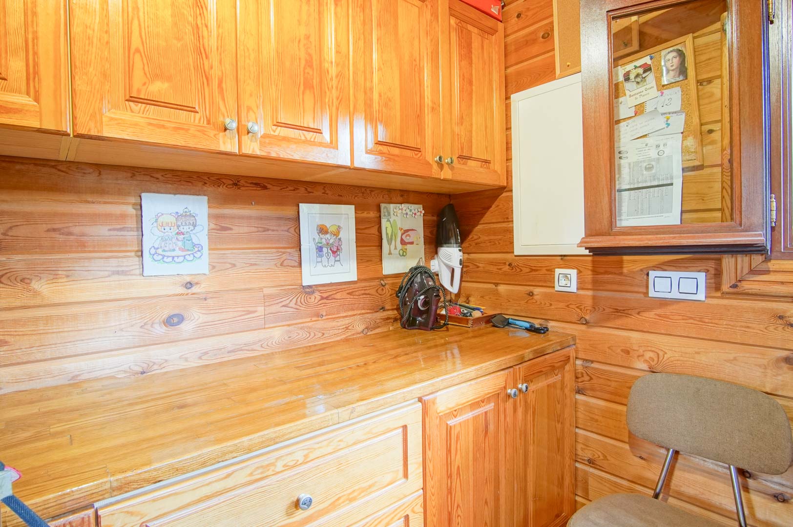 Espace de travail ou cellier revêtu de bois de pin, comprenant des armoires de rangement intégrées et un plan de travail fonctionnel au style rustique.