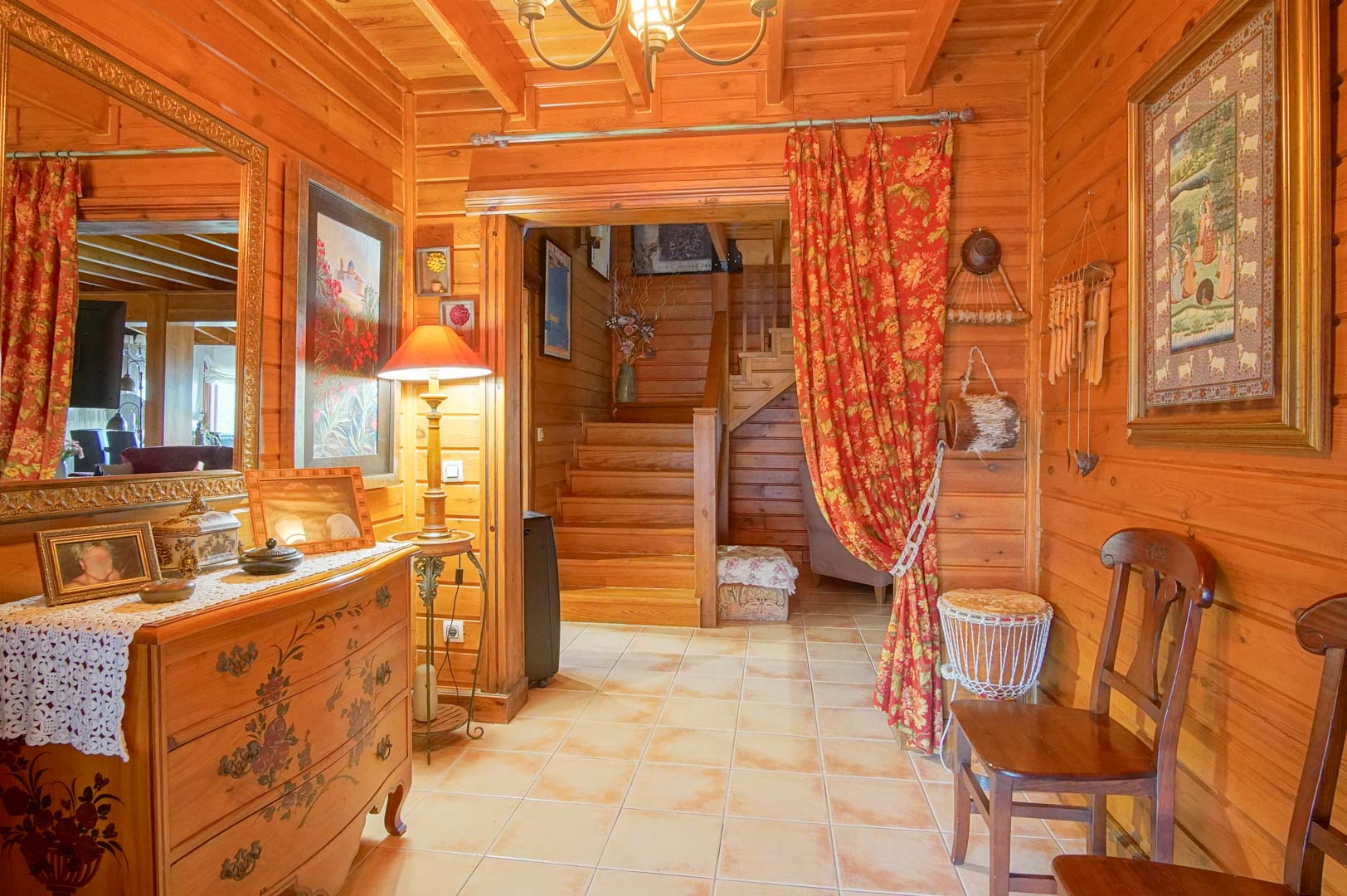 Hall d'entrée rustique avec des murs en pin finlandais, un sol en céramique et un escalier en bois. La décoration chaleureuse souligne le caractère noble des matériaux.