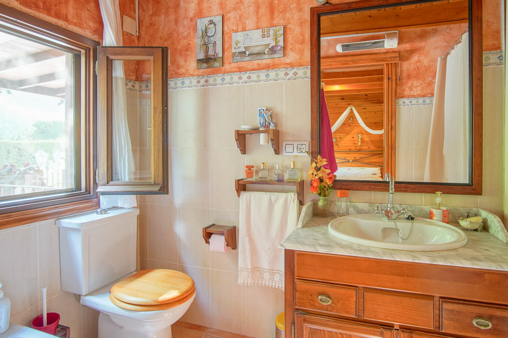 Salle de bain rustique avec meuble en bois, plan de travail en marbre et fenêtre. Le miroir reflète la chambre attenante lambrissée de pin.
