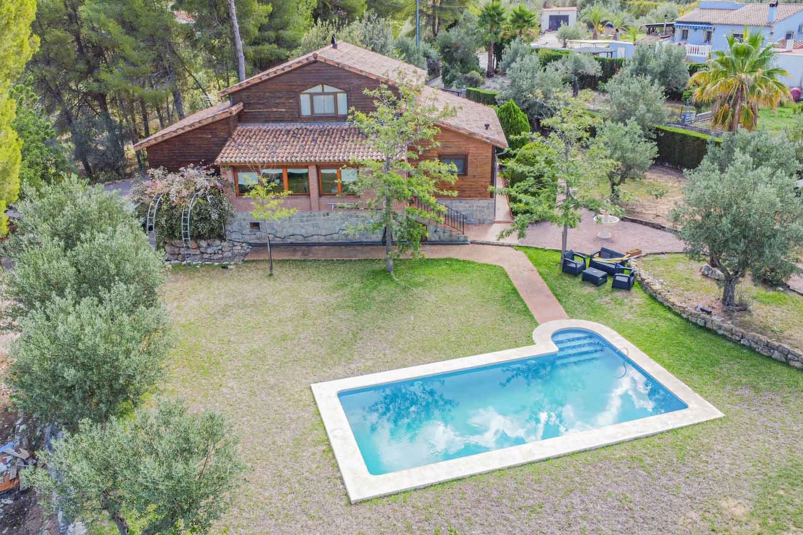 Vue aérienne de la villa en bois et pierre, avec sa piscine privée entourée d'une pelouse et d'un jardin méditerranéen planté d'oliviers.