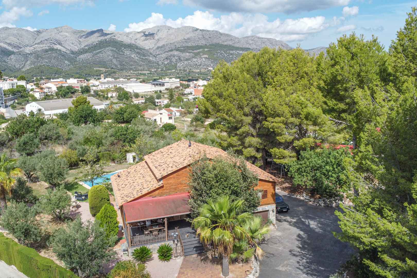 Vue aérienne de la villa en pin finlandais entourée d'un jardin méditerranéen, offrant une vue imprenable sur les montagnes et le village d'Orba.